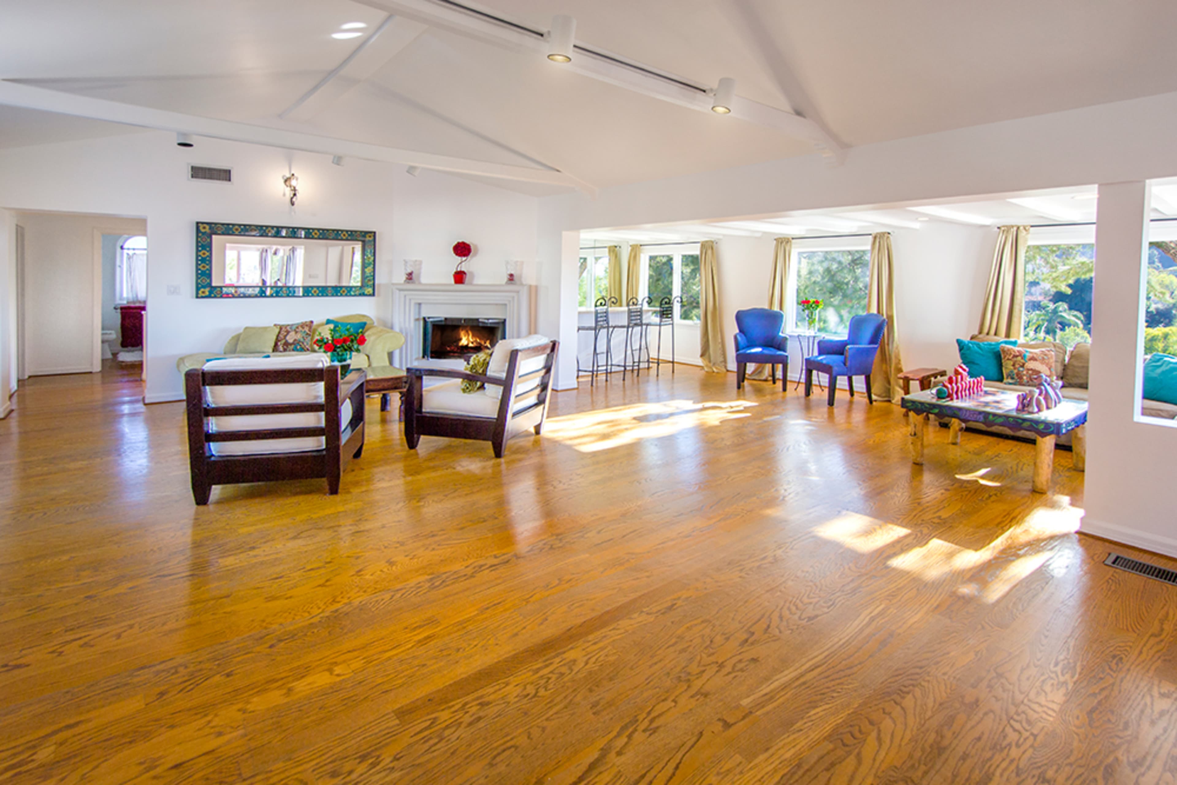A bright, open living space with wooden floors, a fireplace, and large windows allowing natural light to enter.