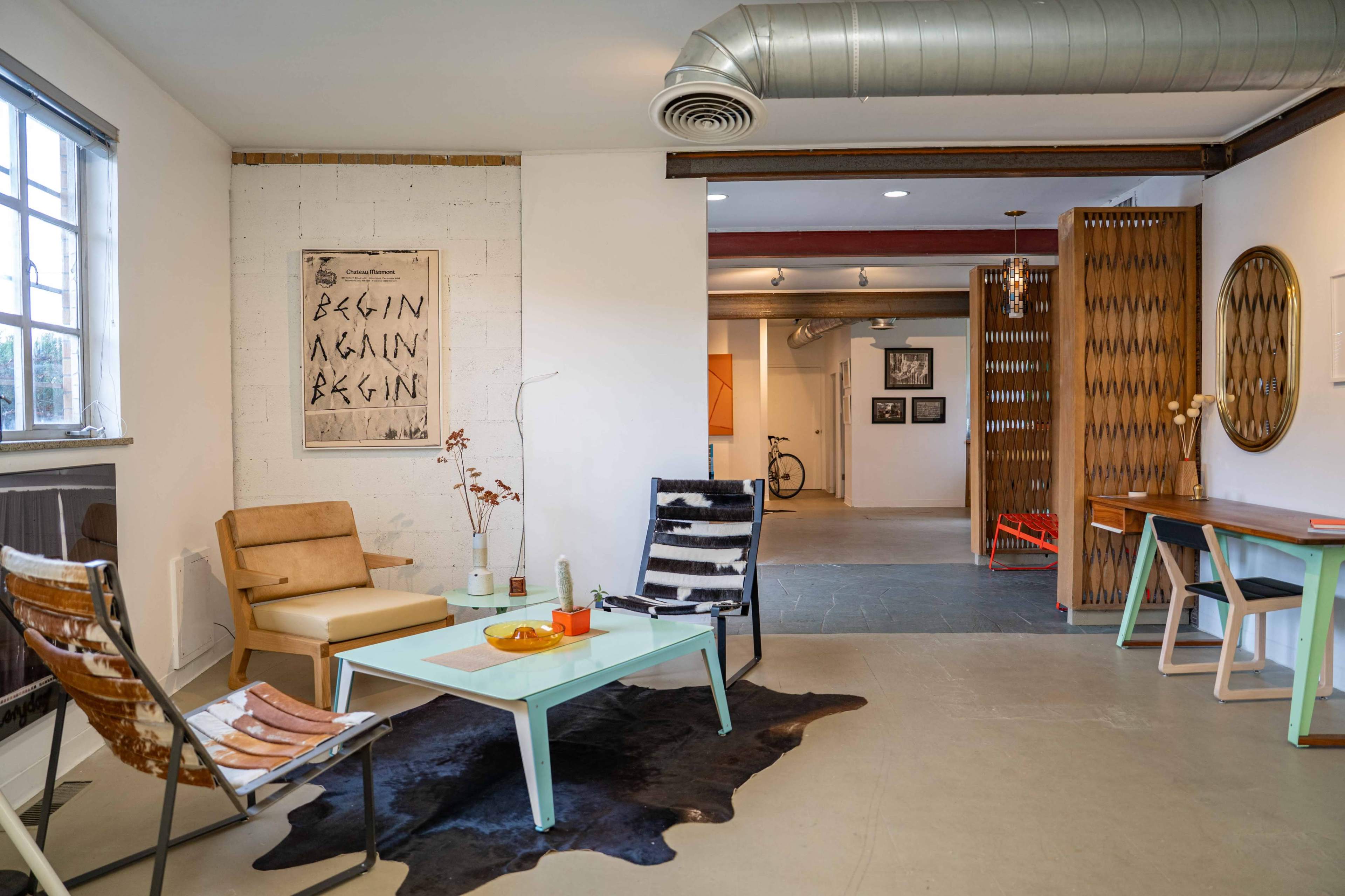 The image shows a modern interior space with a seating area featuring two chairs, a green coffee table, and decorative elements like a cowhide rug and wall art.