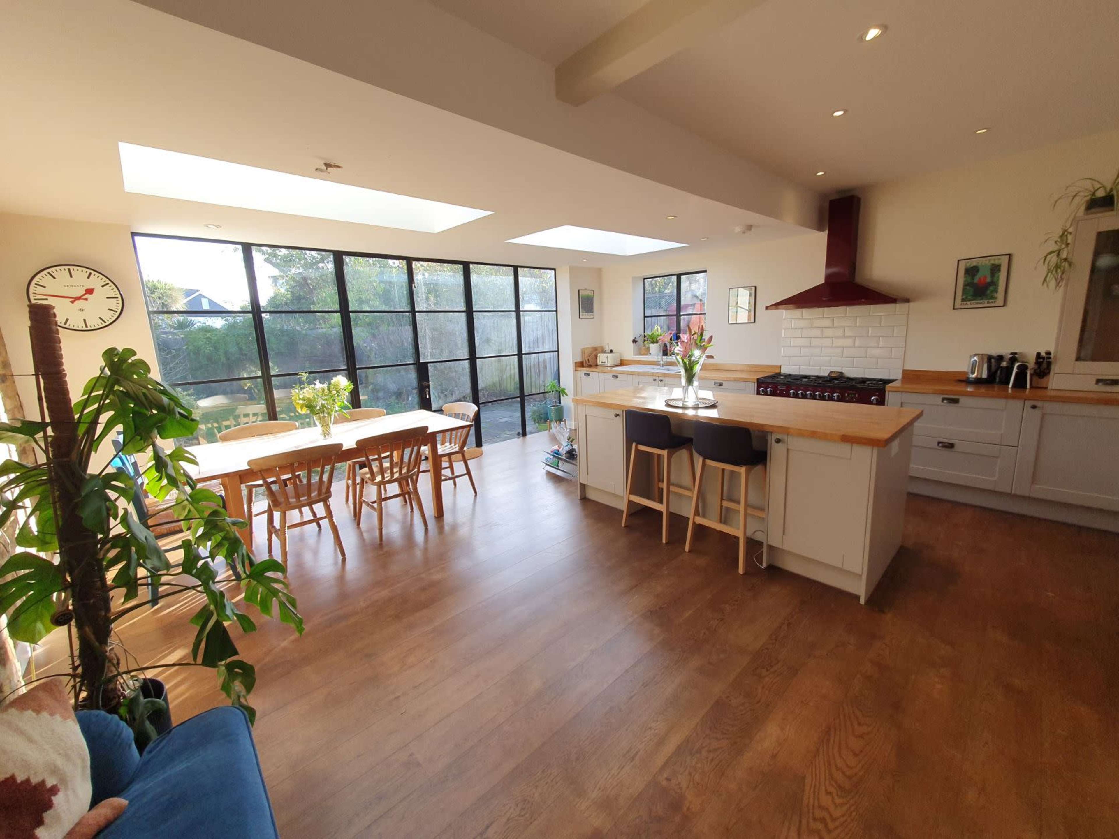 A spacious kitchen features a large island with seating, a wooden dining table, and large windows allowing natural light to fill the room.