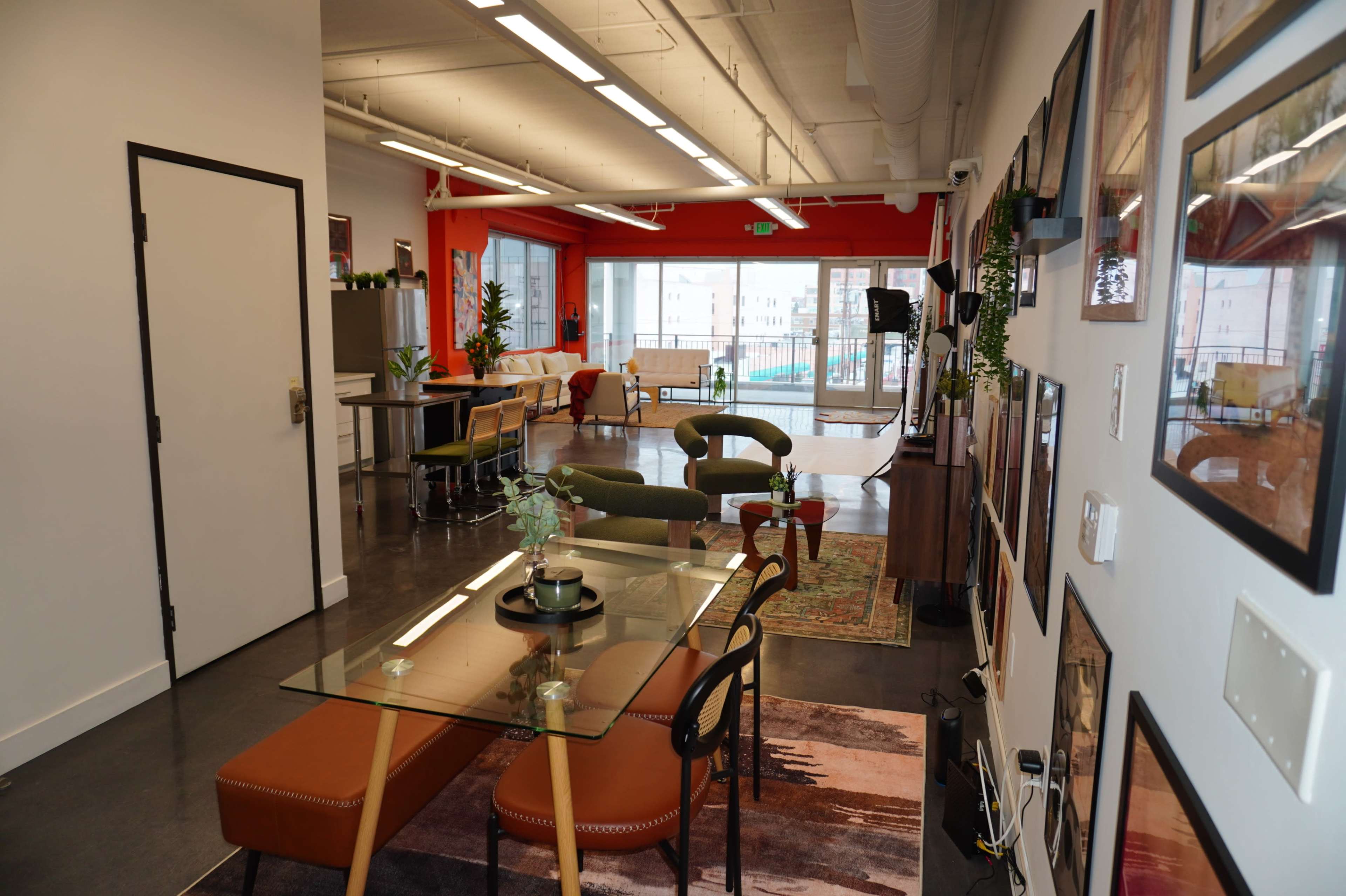 The image shows a modern open-concept office space featuring a dining table, lounge seating, and large windows that let in natural light.