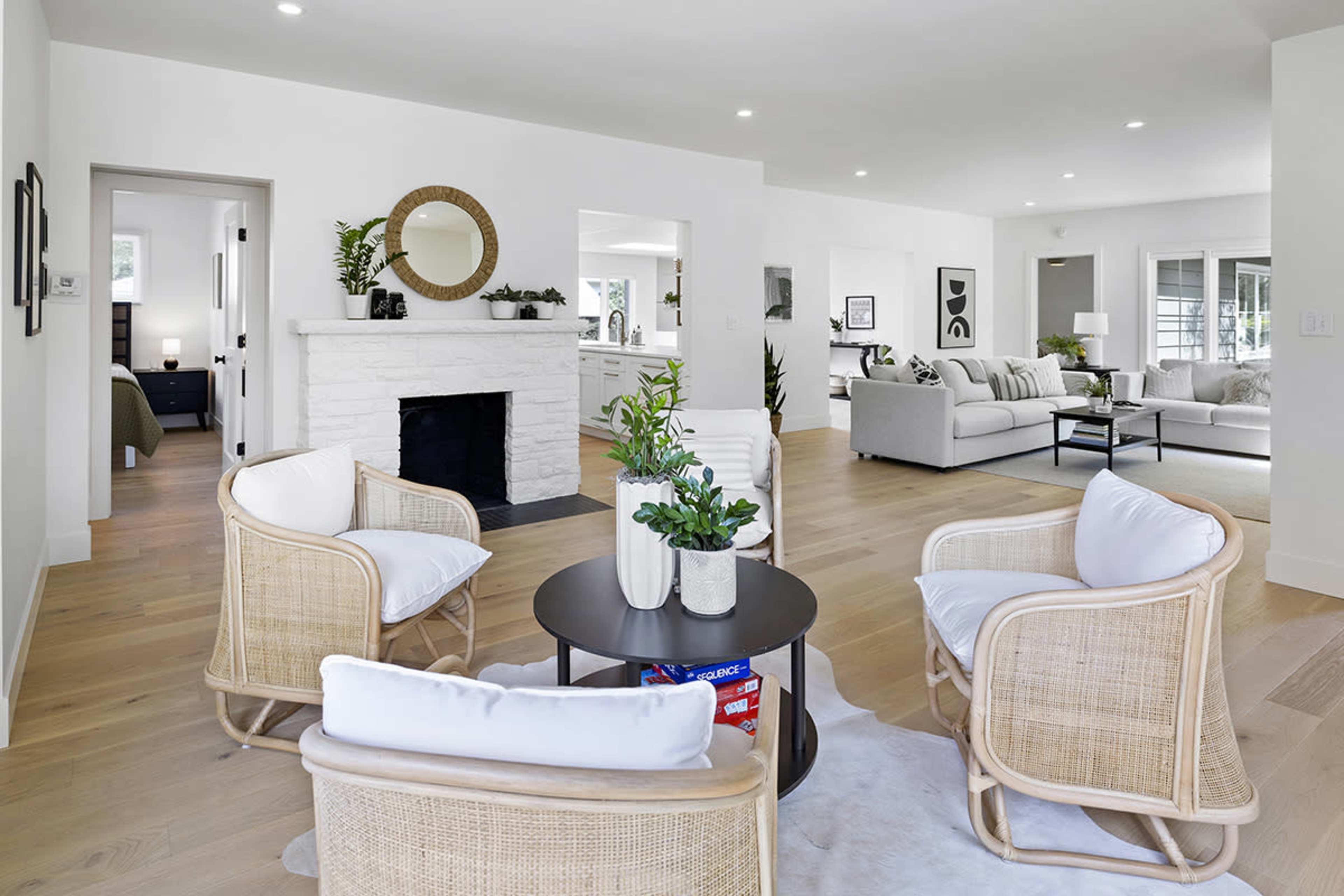 A bright, modern living room featuring two woven chairs positioned around a small black table, with a white stone fireplace in the background.
