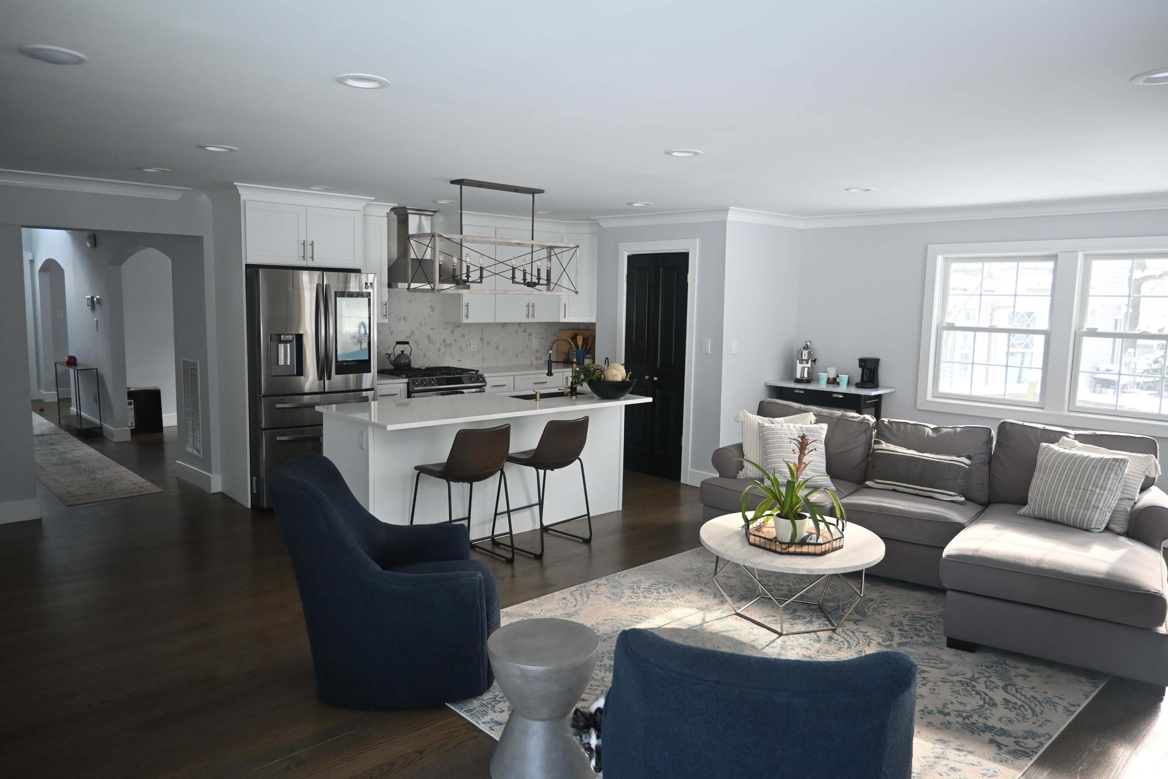 A modern open-concept living space features a kitchen with a central island and bar stools, adjacent to a cozy seating area with a sectional sofa and decorative accents.