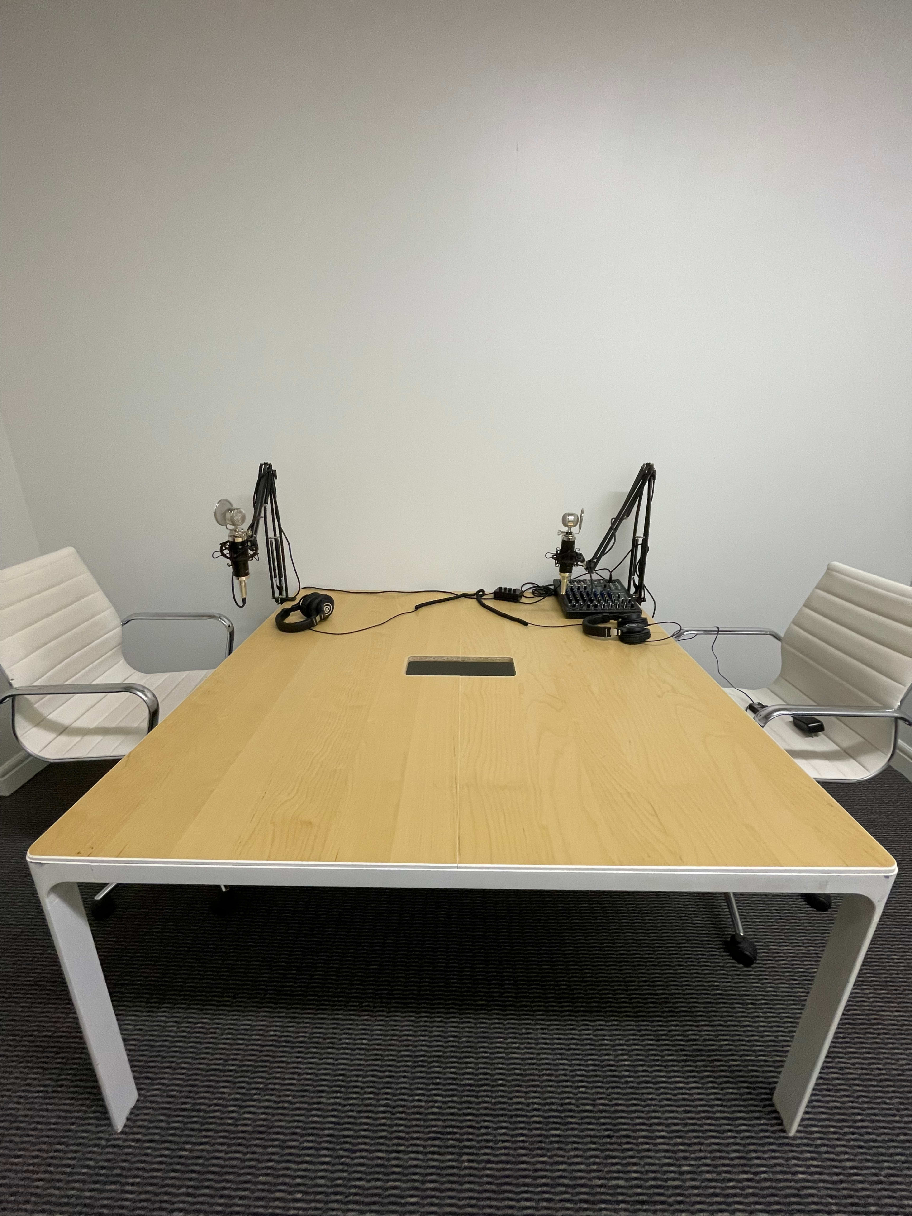 A clean, empty conference room features a large wooden table with two microphones and headsets on either side.