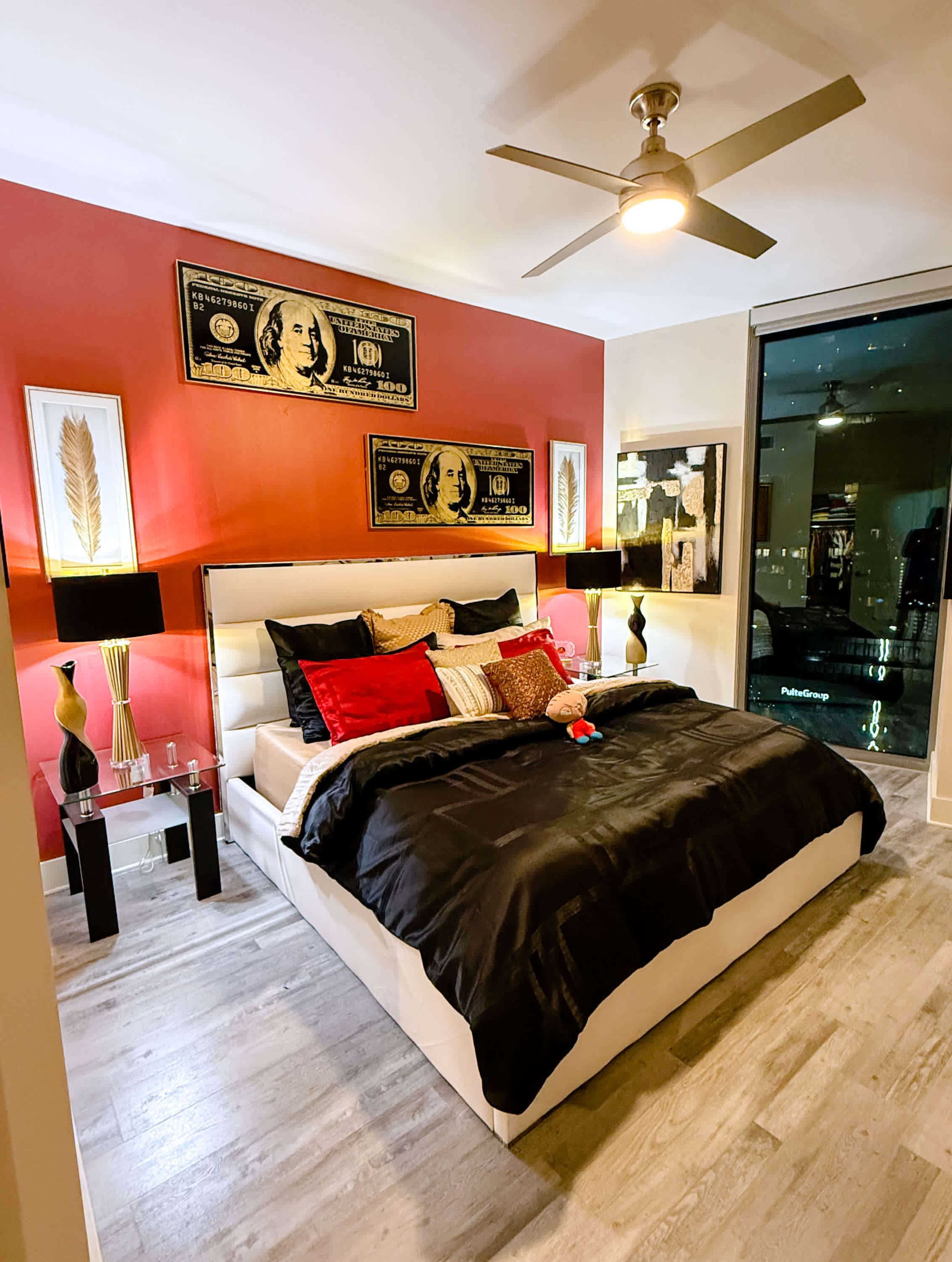 The bedroom features a large bed with dark bedding, decorative pillows, two black lamps on nightstands, and bold red accent walls.