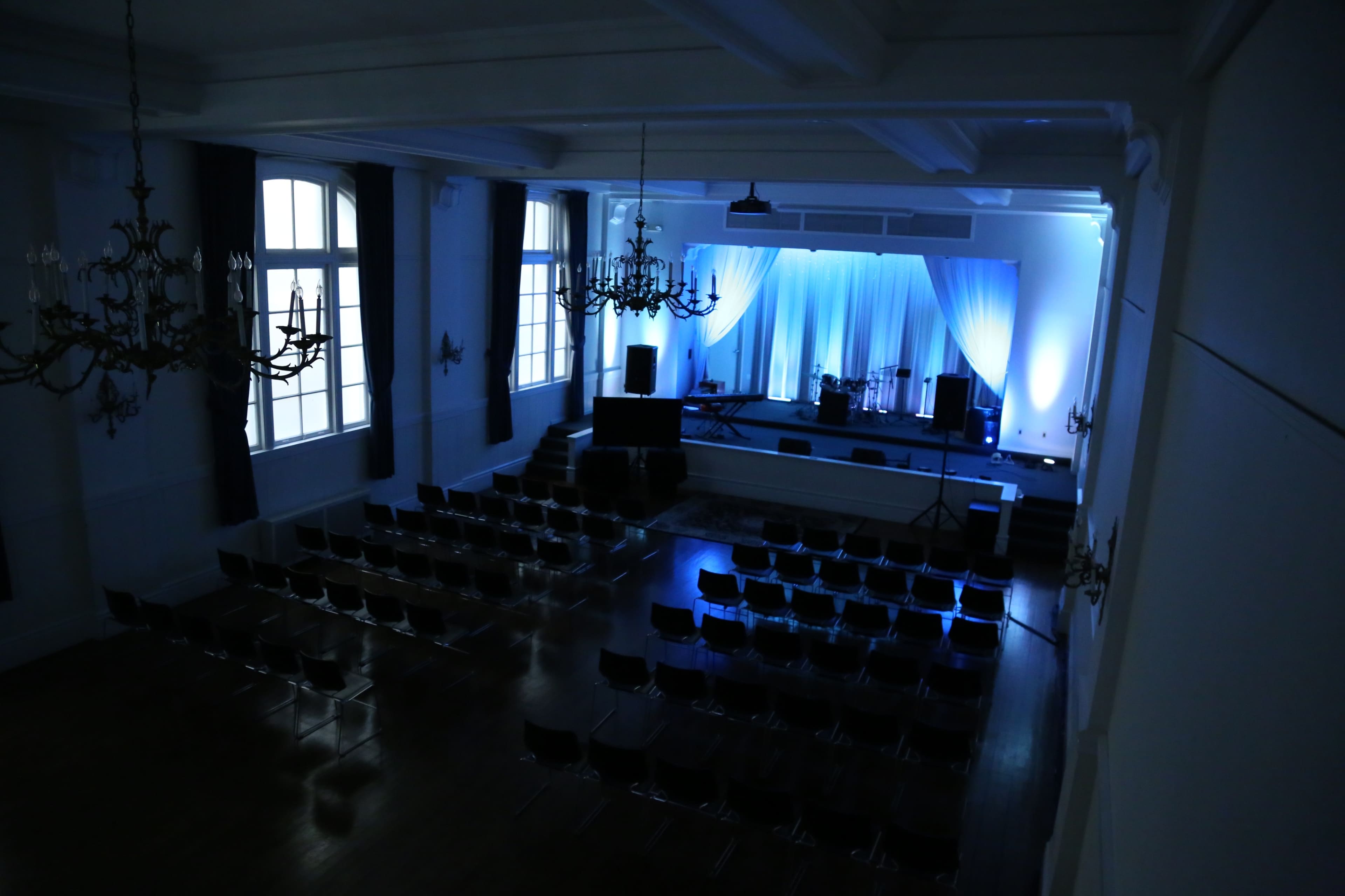 A spacious auditorium with rows of chairs facing a stage adorned with blue lighting and a white backdrop.