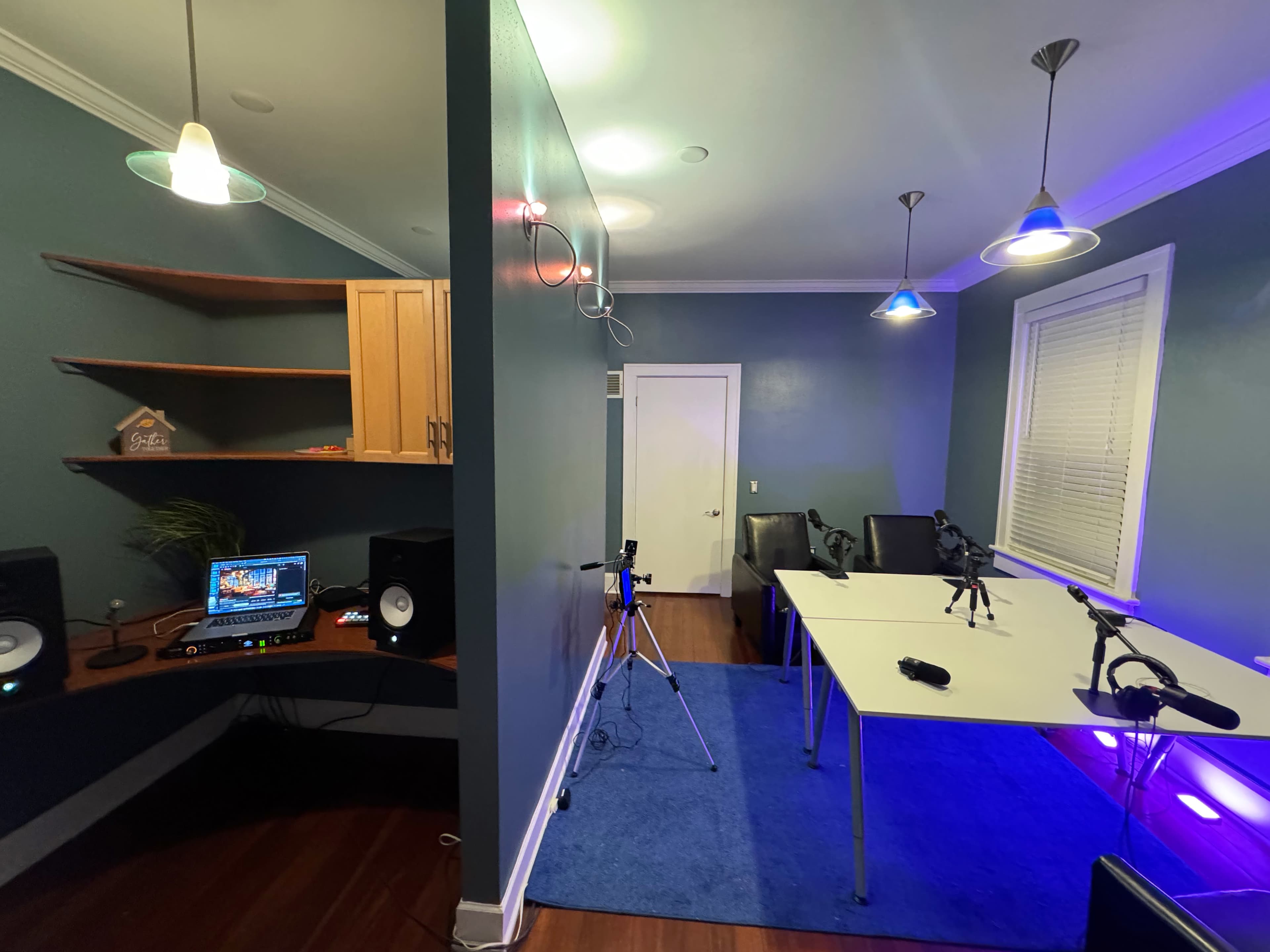 A modern room setup with a desk, audio equipment, a blue carpet, and a white table equipped with recording devices.