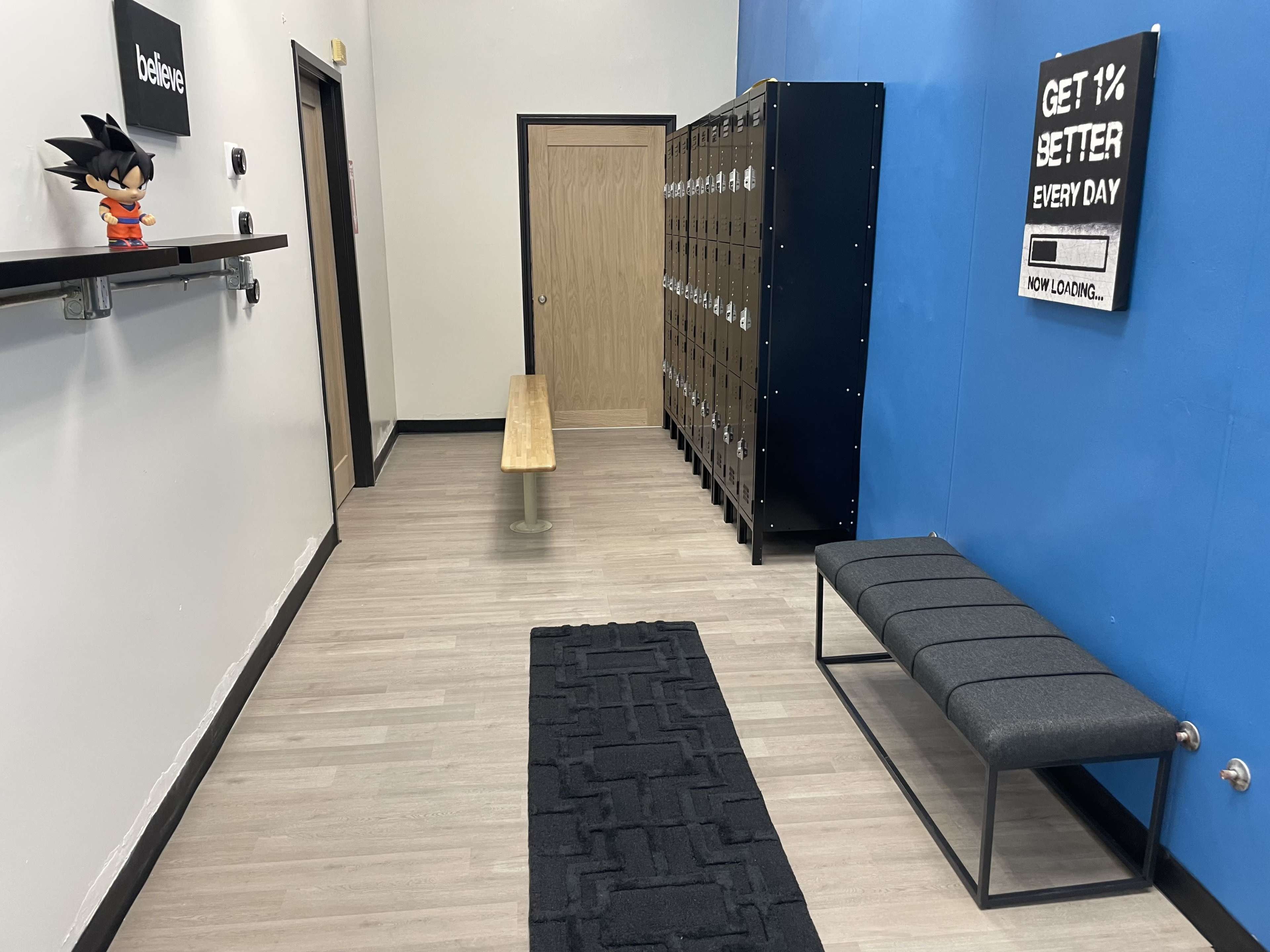 The image shows a hallway with a bench, lockers against the wall, a shelf displaying a figure, and a motivational sign on a blue wall.