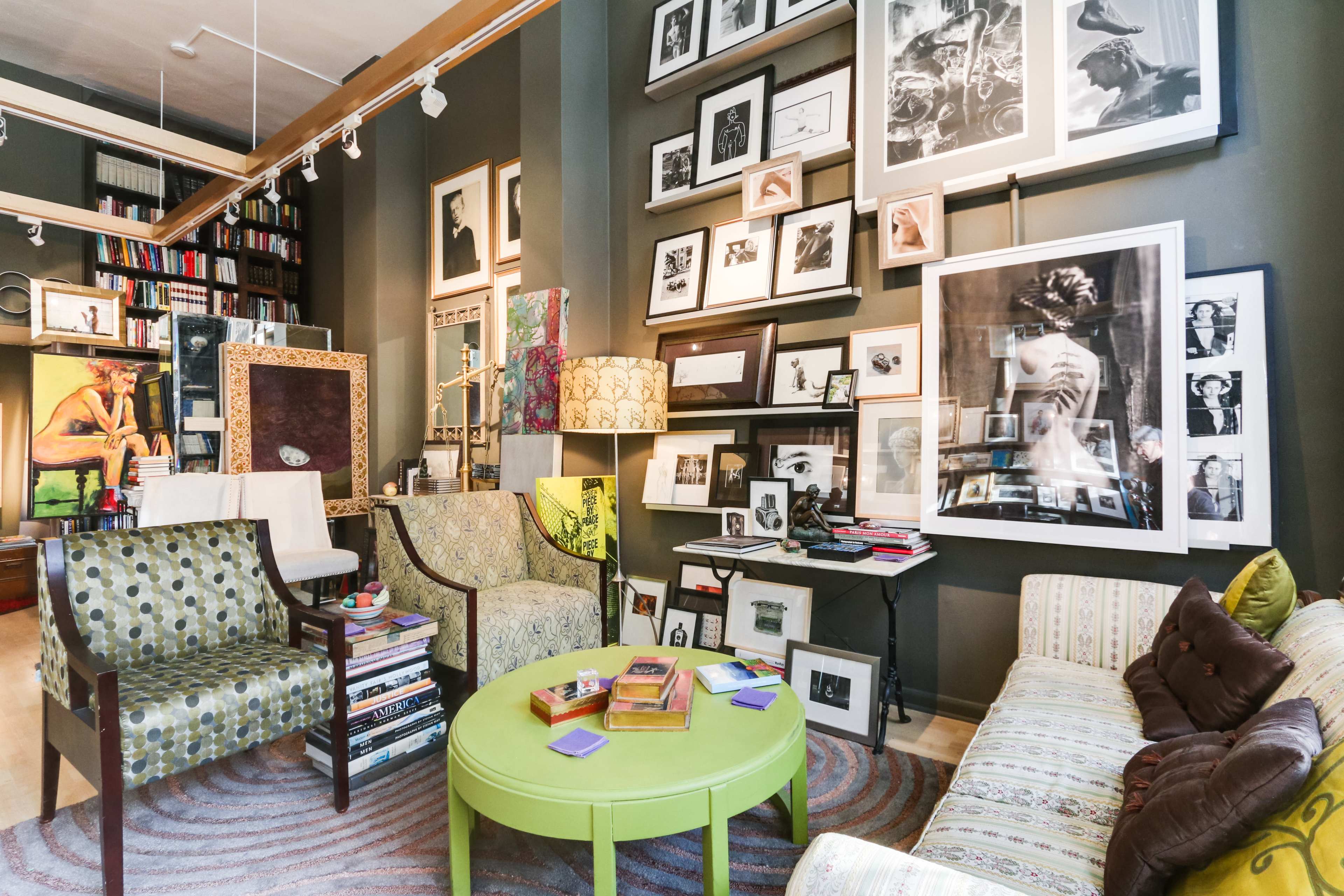 A cozy living room or gallery space filled with framed artwork and photographs, featuring several seating areas with green and patterned furniture.