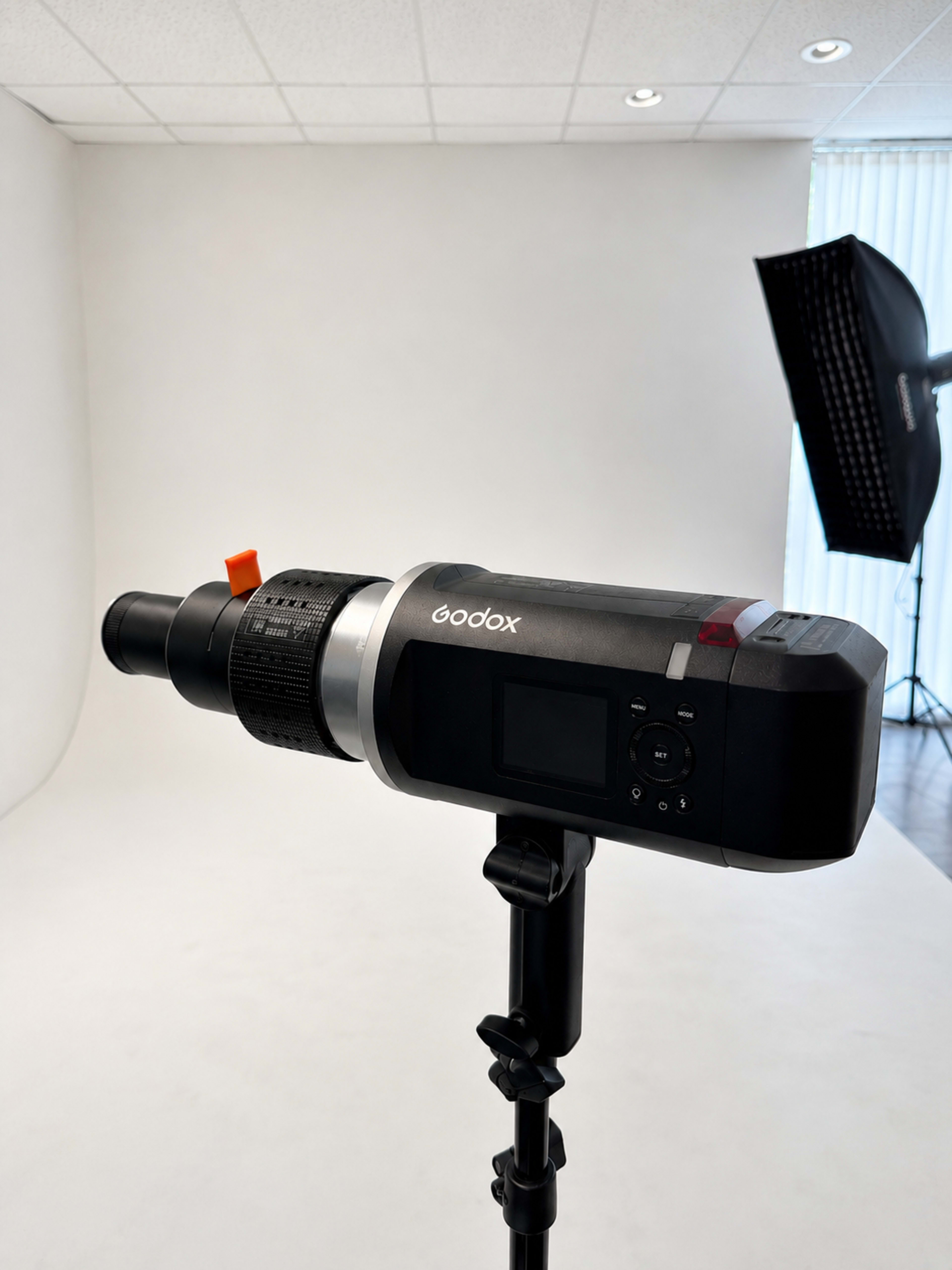 The image shows a Godox studio light mounted on a stand, positioned in front of a plain white backdrop with a large softbox nearby.