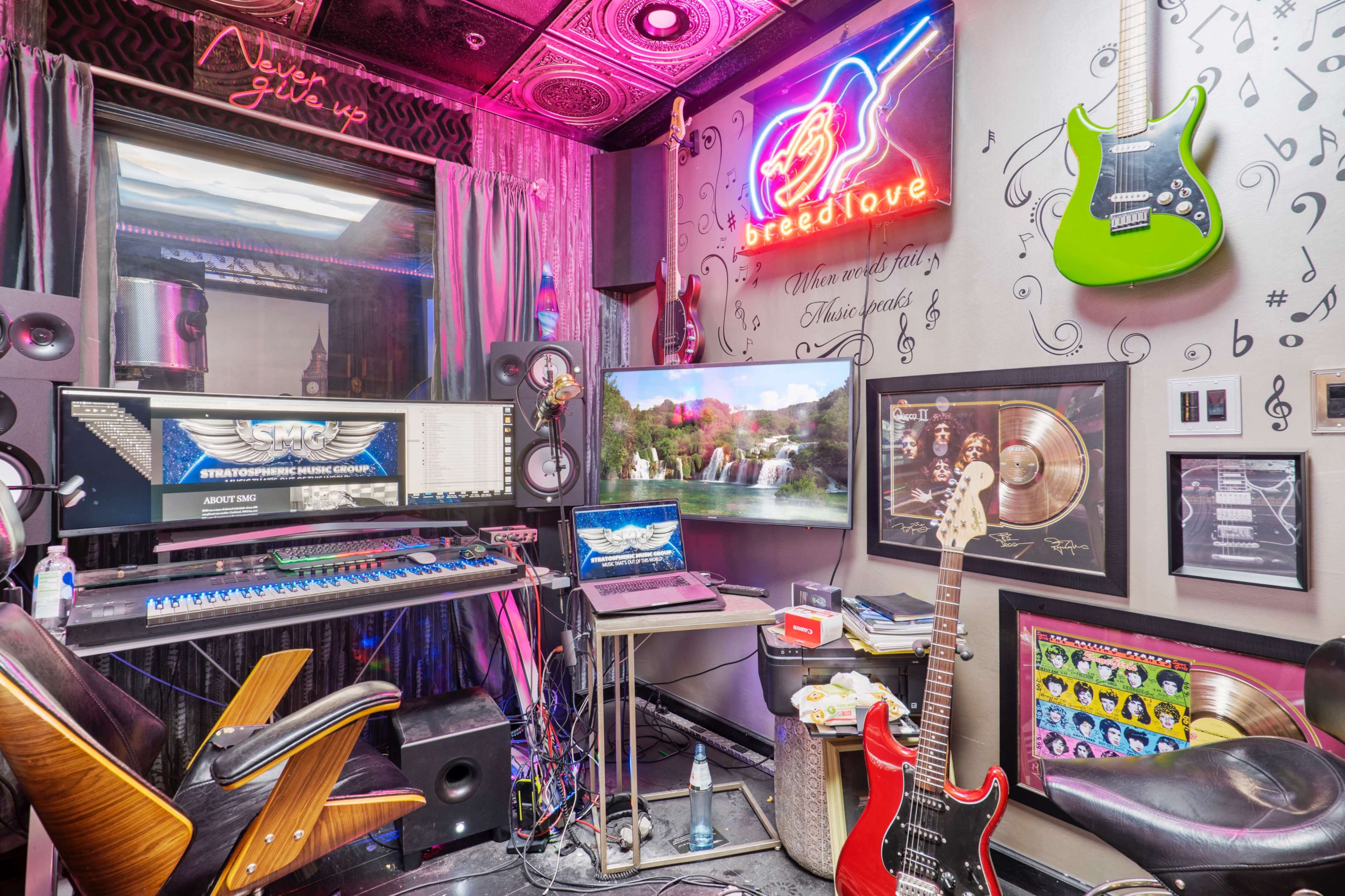 The image shows a vibrant music production room featuring guitars, a computer setup with monitors, and various music-themed decorations.