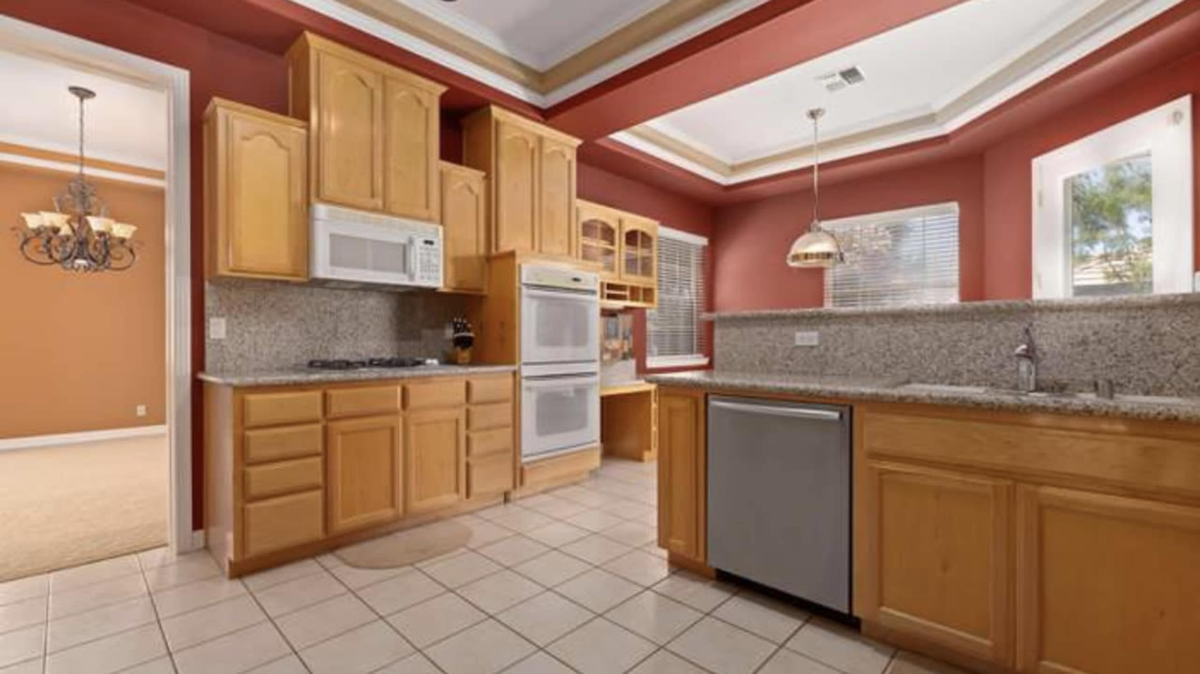 A kitchen featuring wooden cabinetry, granite countertops, and appliances including a microwave and a refrigerator.
