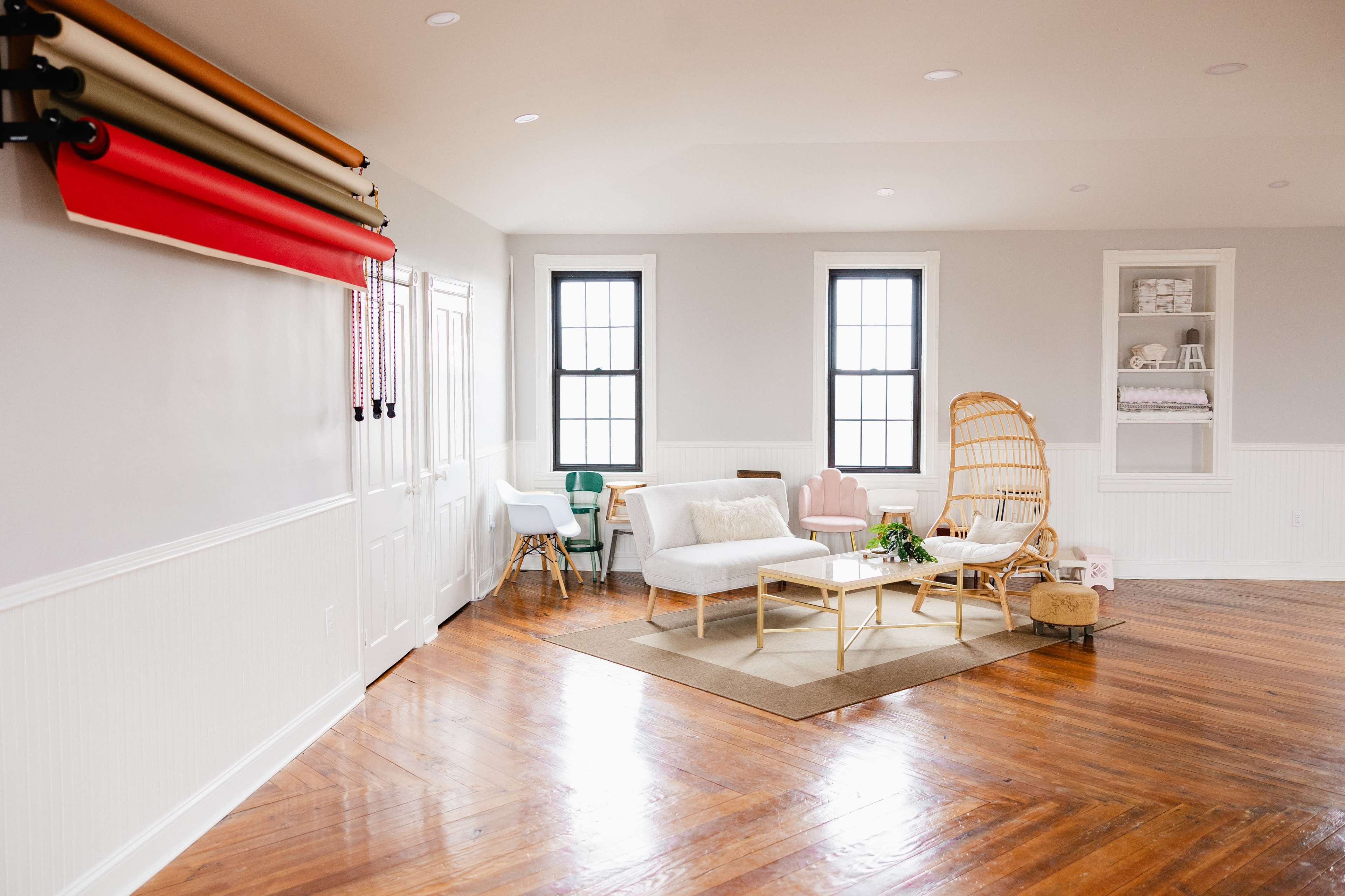 A bright, open living space featuring a combination of seating options, wooden flooring, and colorful backdrop rolls.