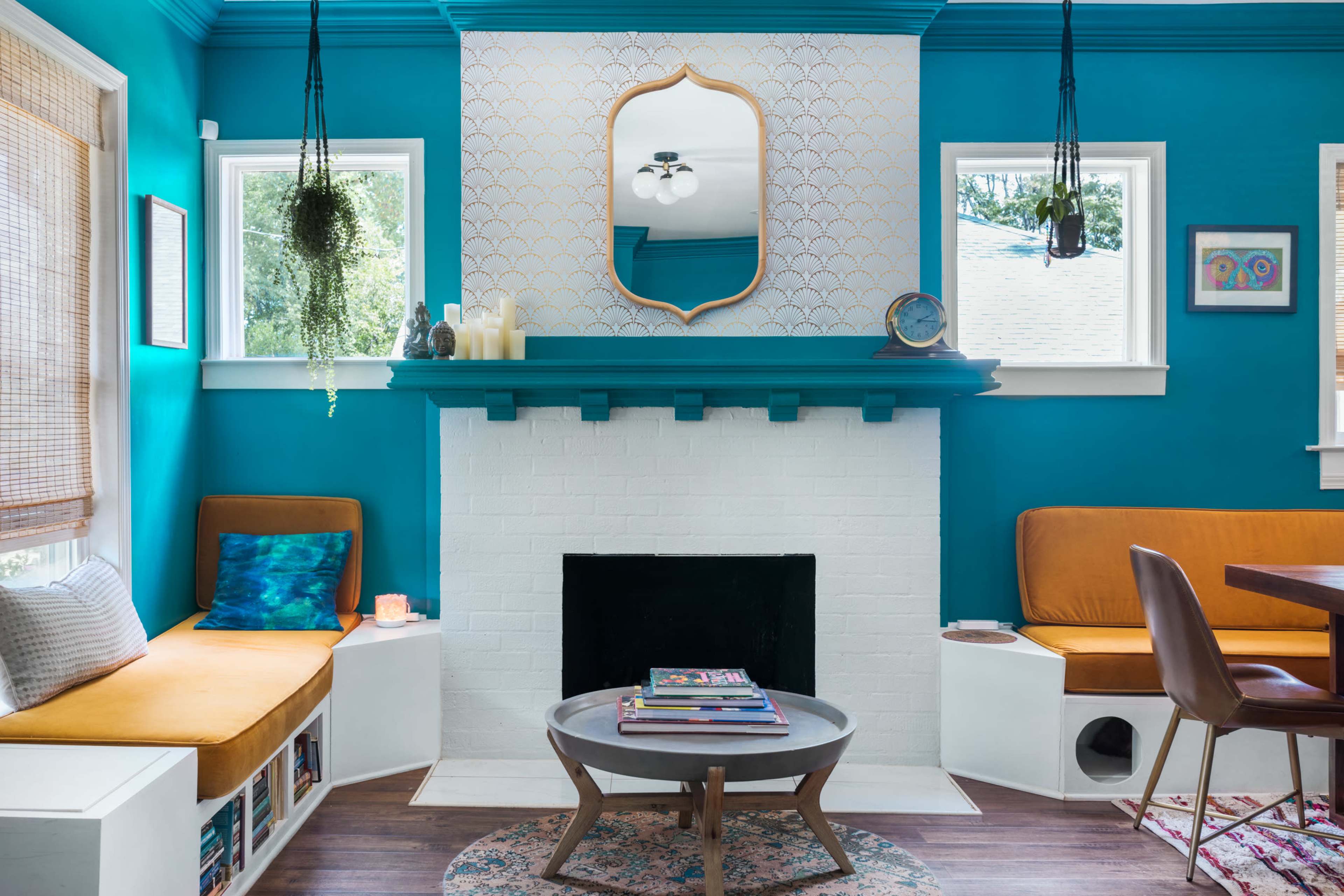 The room features a bright blue wall with a mirrored mantel above a white brick fireplace, flanked by large windows and decorated with comfortable seating and a round coffee table.