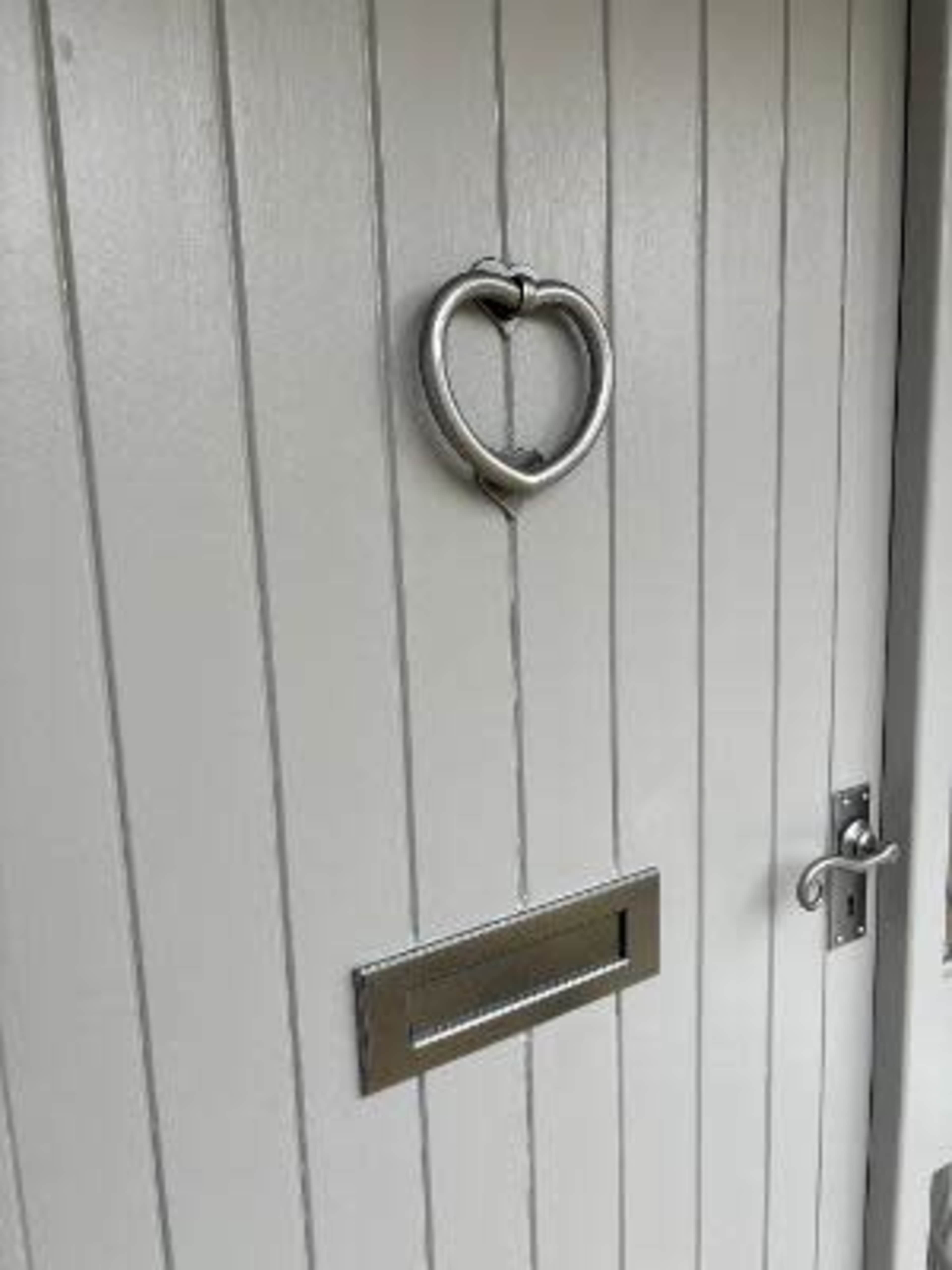 A heart-shaped knocker is mounted on a gray wooden door with a mail slot below it.