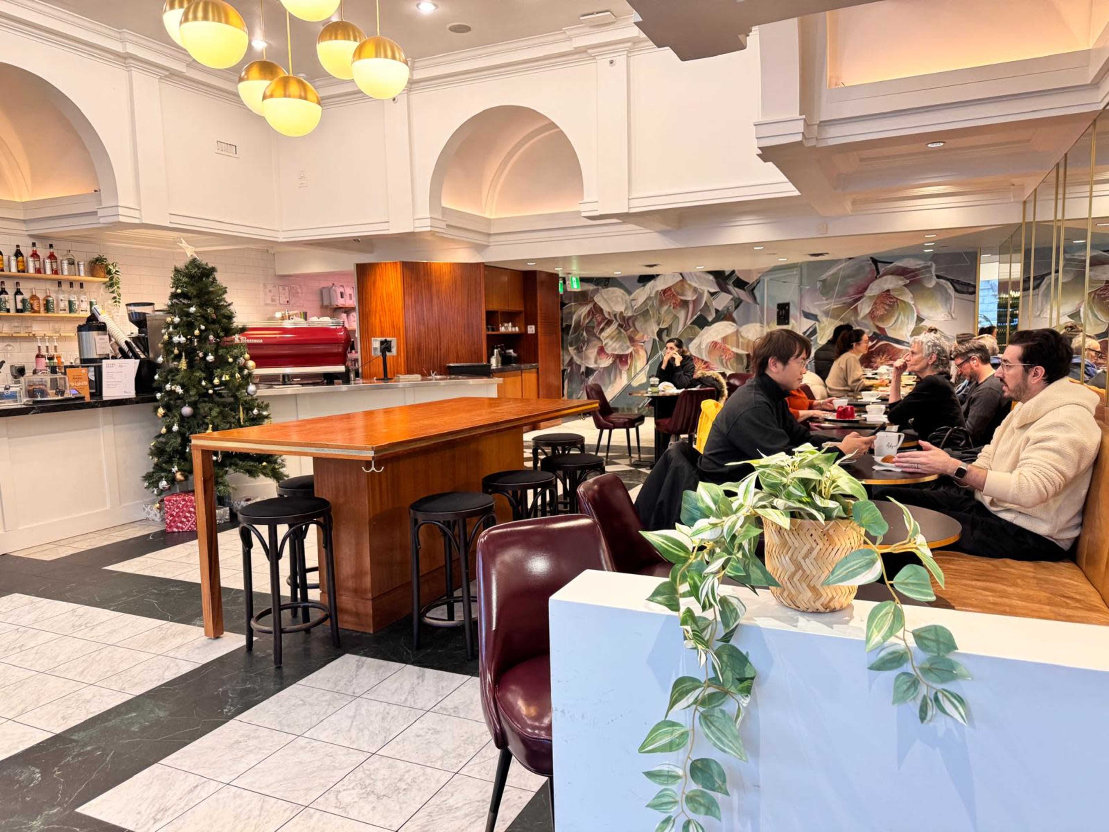 The image shows a cozy café interior with a coffee bar, seating area, and a decorated Christmas tree in the corner.