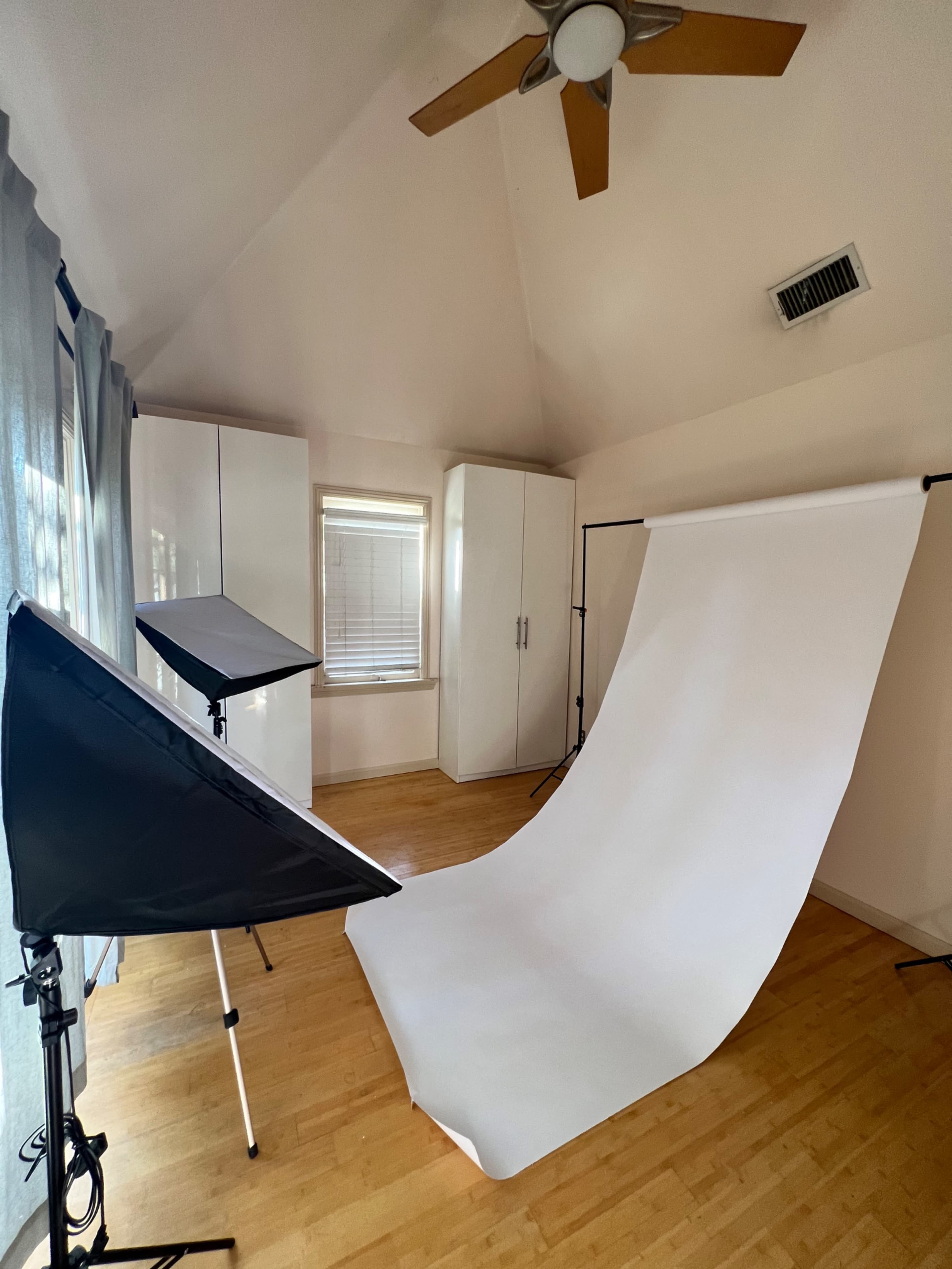 A photo studio with a white backdrop, softbox lighting, and wooden flooring.