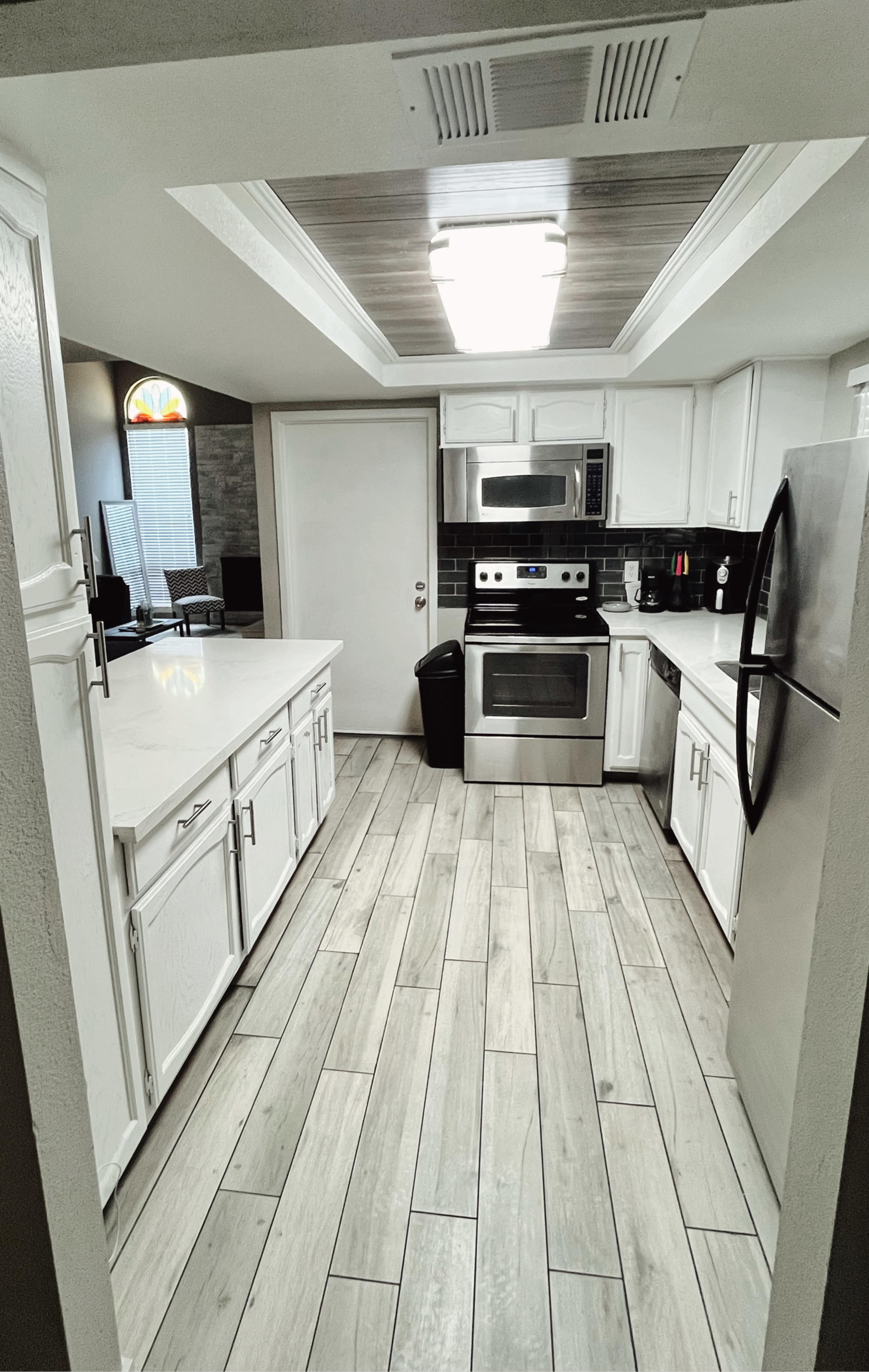 A modern kitchen with white cabinets, stainless steel appliances, and a tile floor featuring a wood-like appearance.