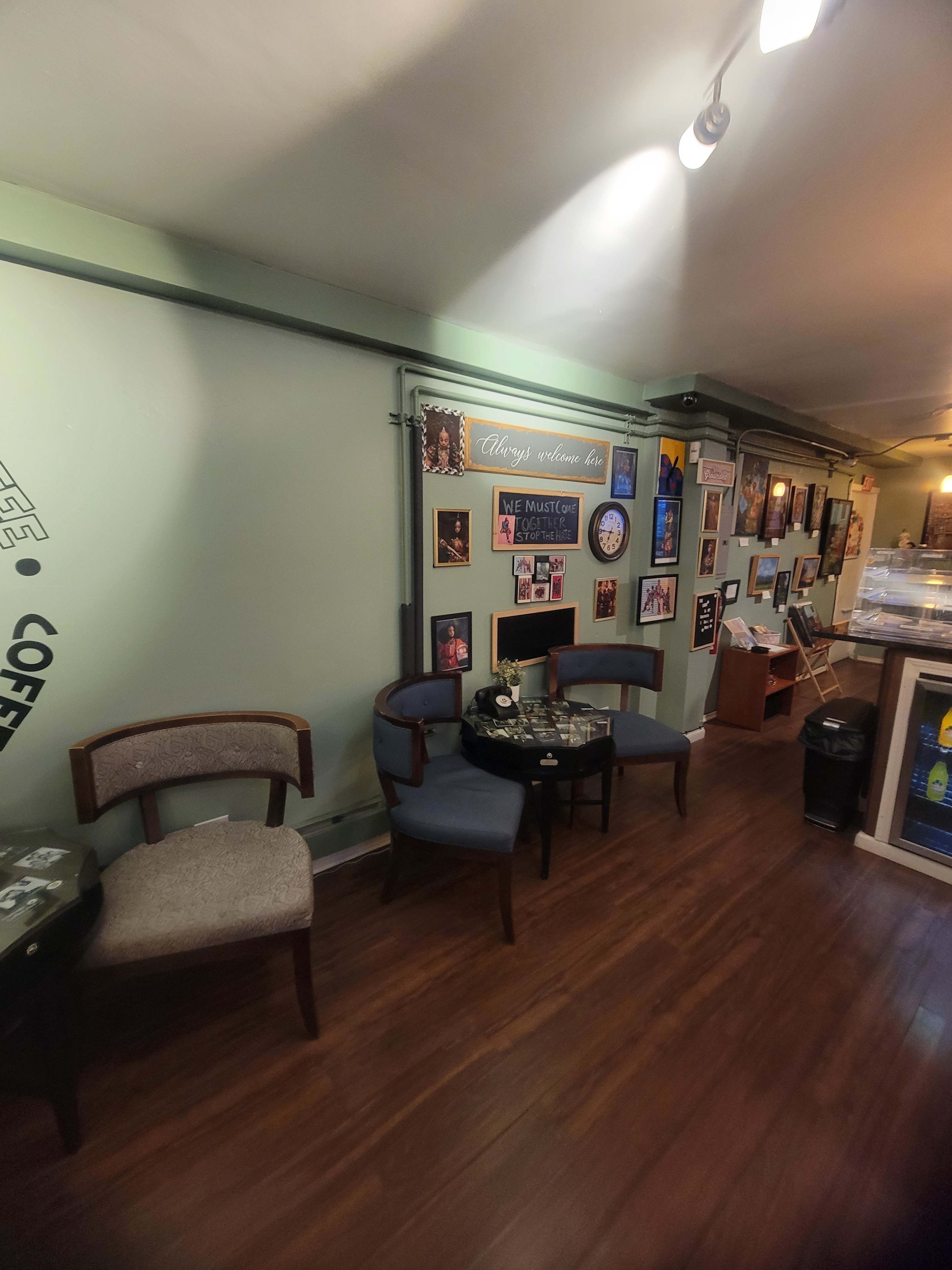 The image shows a cozy coffee shop corner with two chairs, a small table, and walls adorned with various framed photographs and decorations.