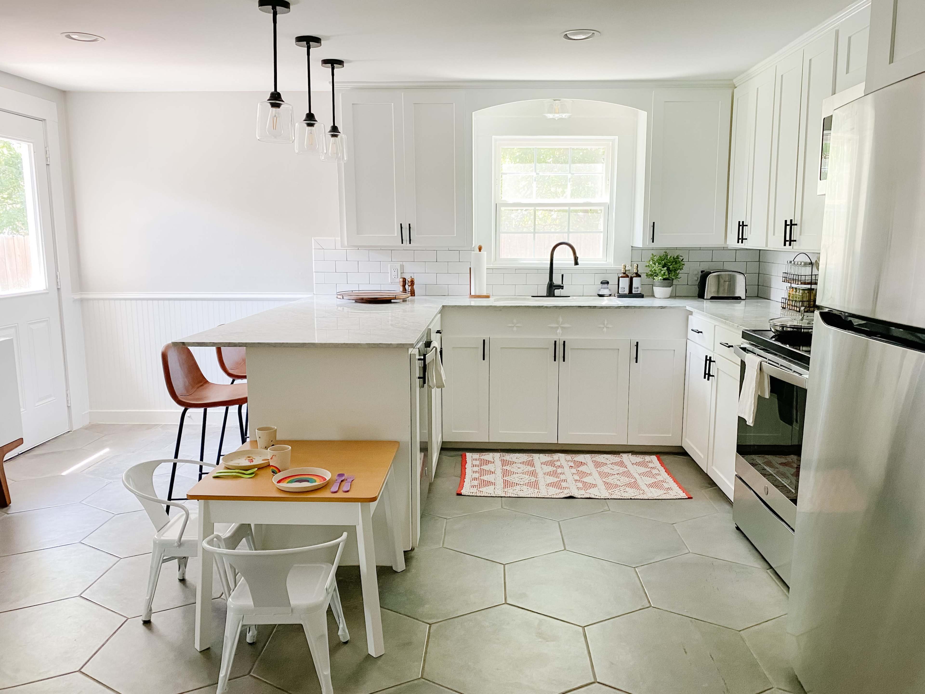 A modern kitchen featuring white cabinets, a central island, and a small table with chairs for children.