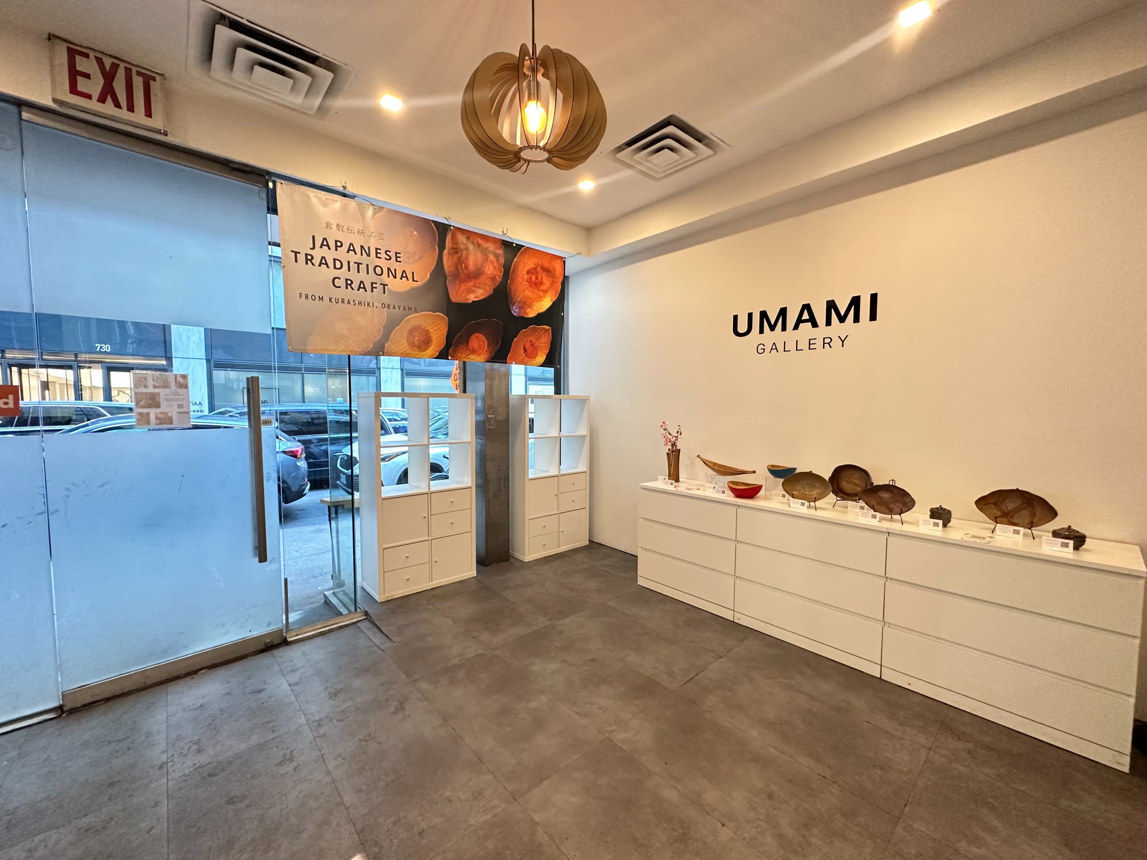 The interior of Umami Gallery, featuring a minimalist design with a large banner about Japanese traditional craft and display cases along the wall.