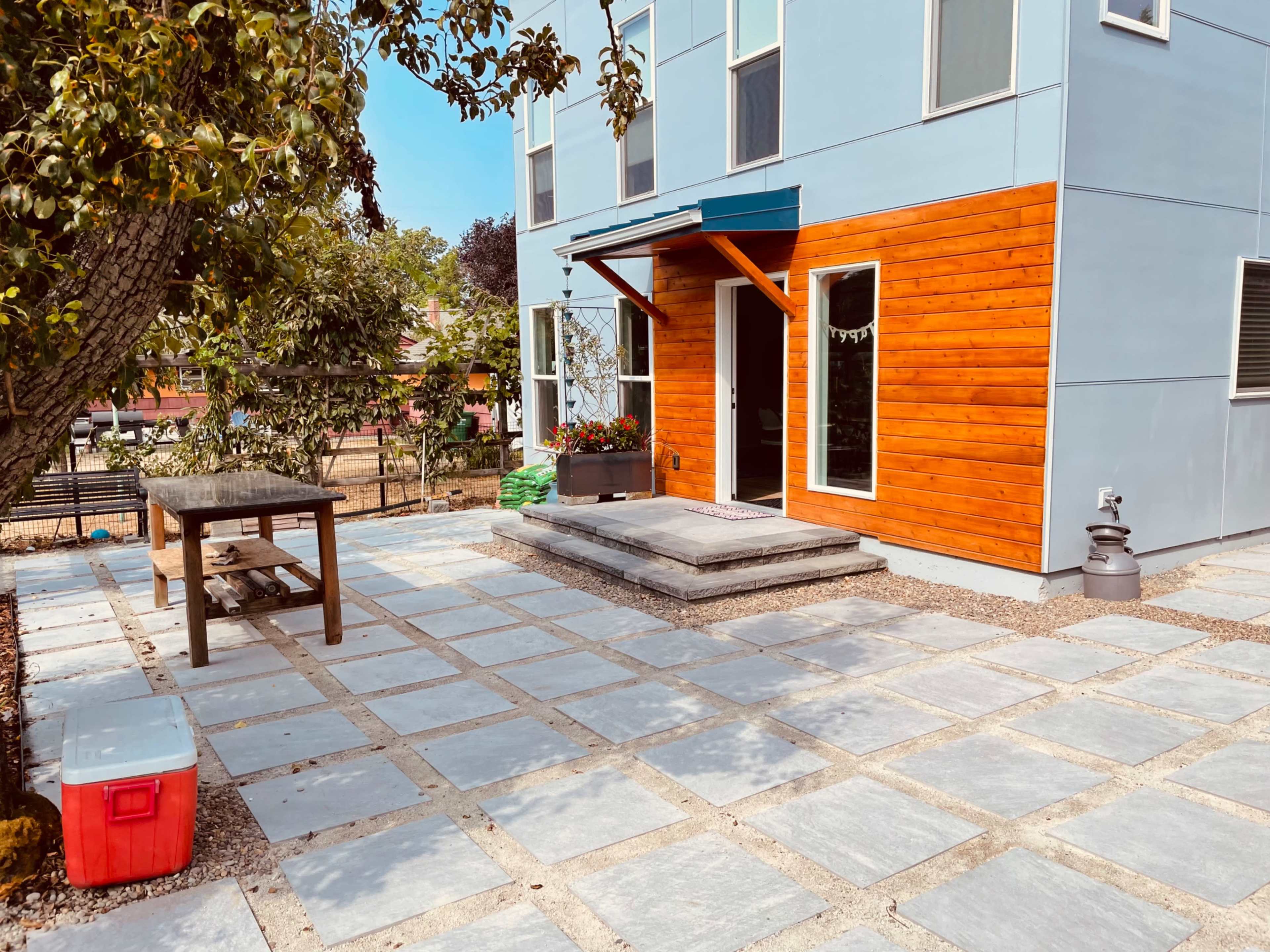 A patio area with large stone tiles in front of a two-toned house featuring wood accents and a blue awning.