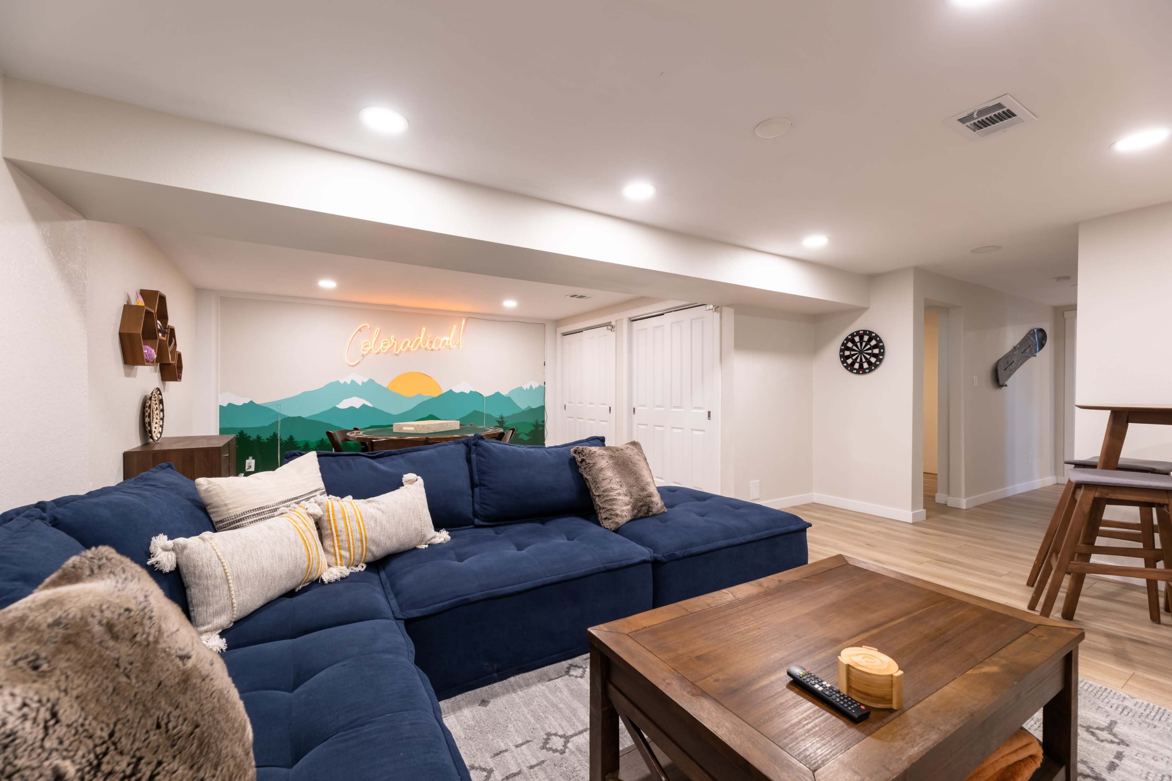 A cozy living room features a dark blue sectional sofa, a wooden coffee table, and a brightly lit wall with a mountain mural and the word "Celebration."