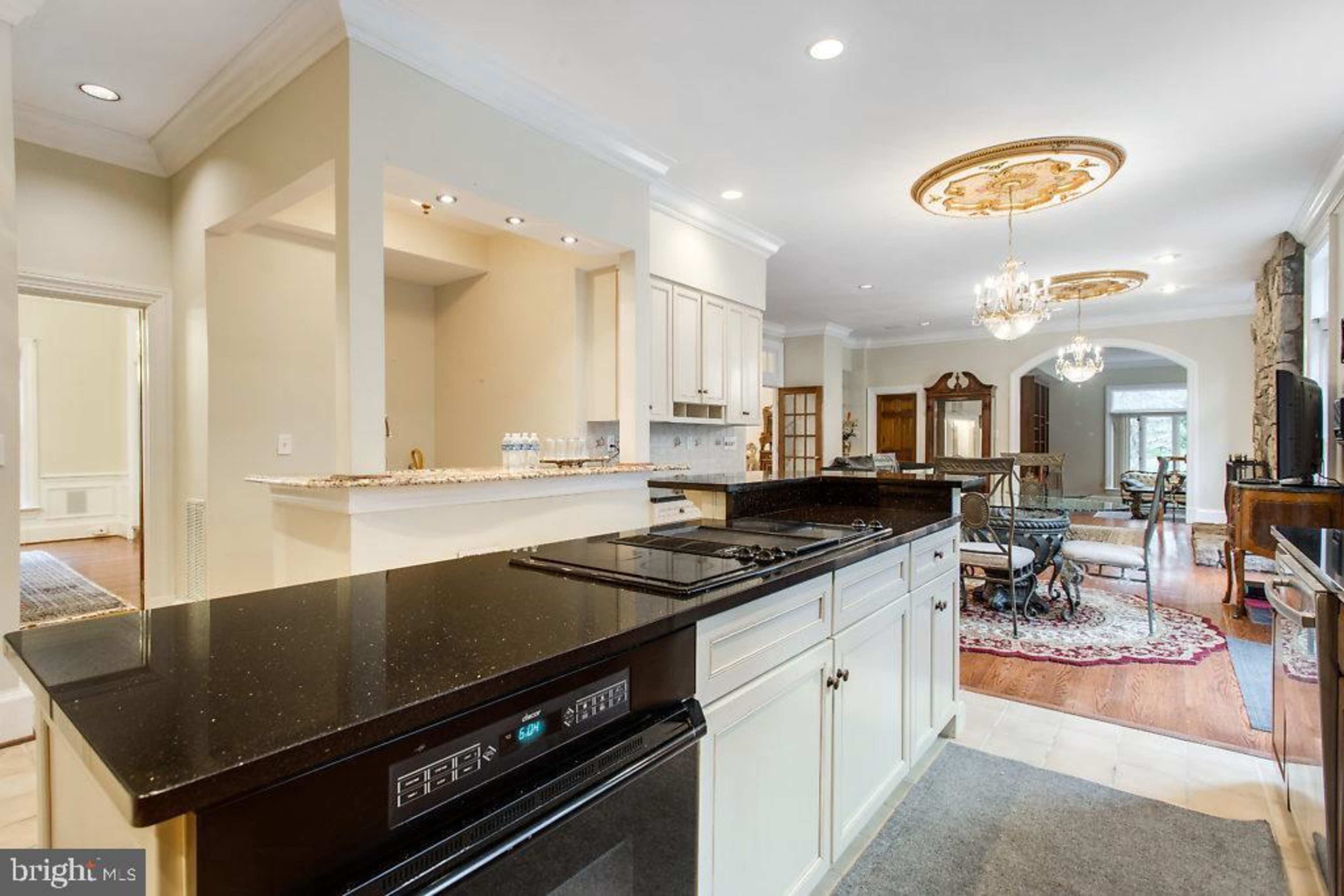 The kitchen features dark countertops, white cabinetry, and is open to a dining area with a chandelier.