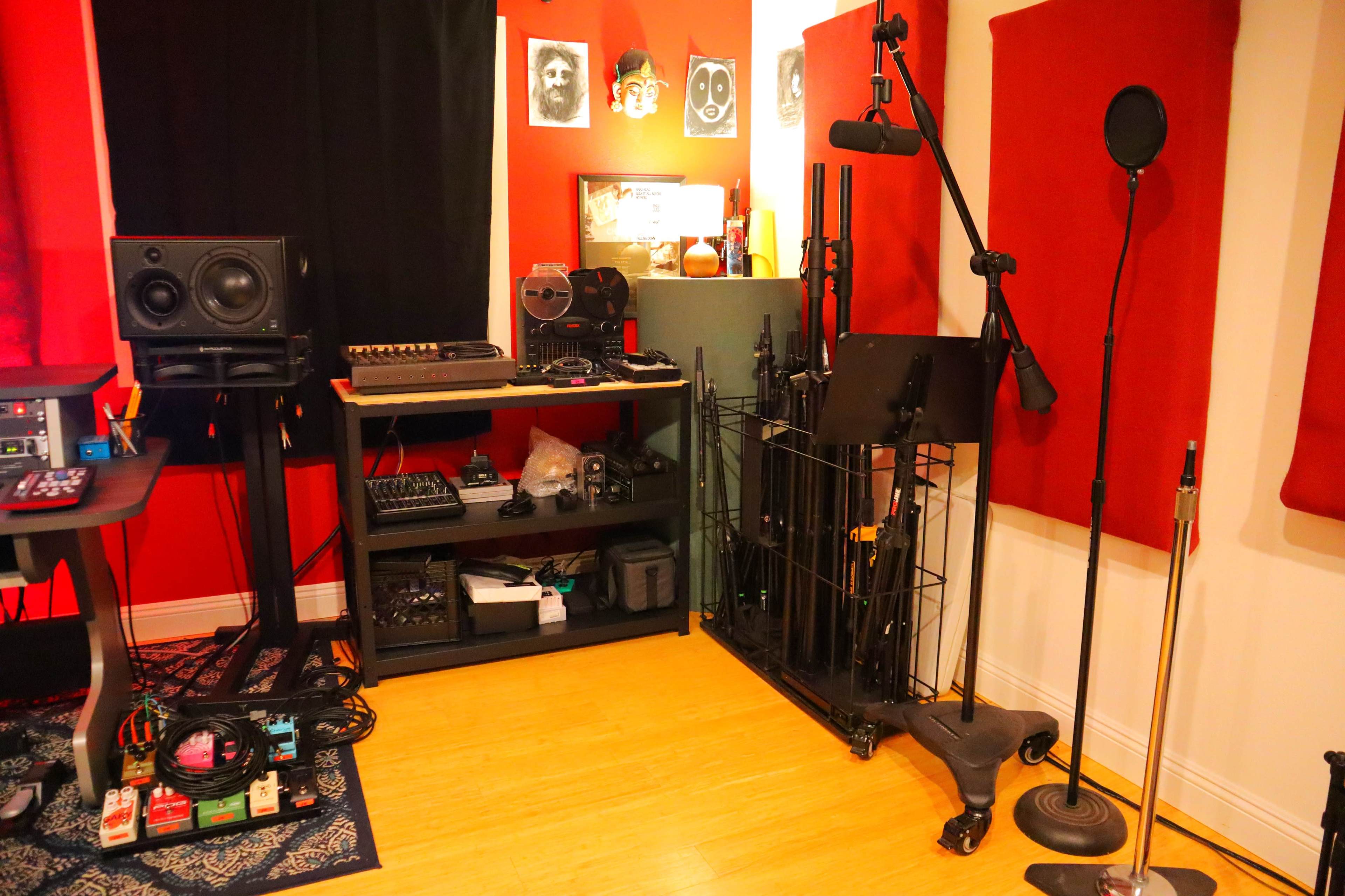 The image shows a music recording studio with audio equipment, including speakers, a keyboard, and microphones, set against red and black walls.