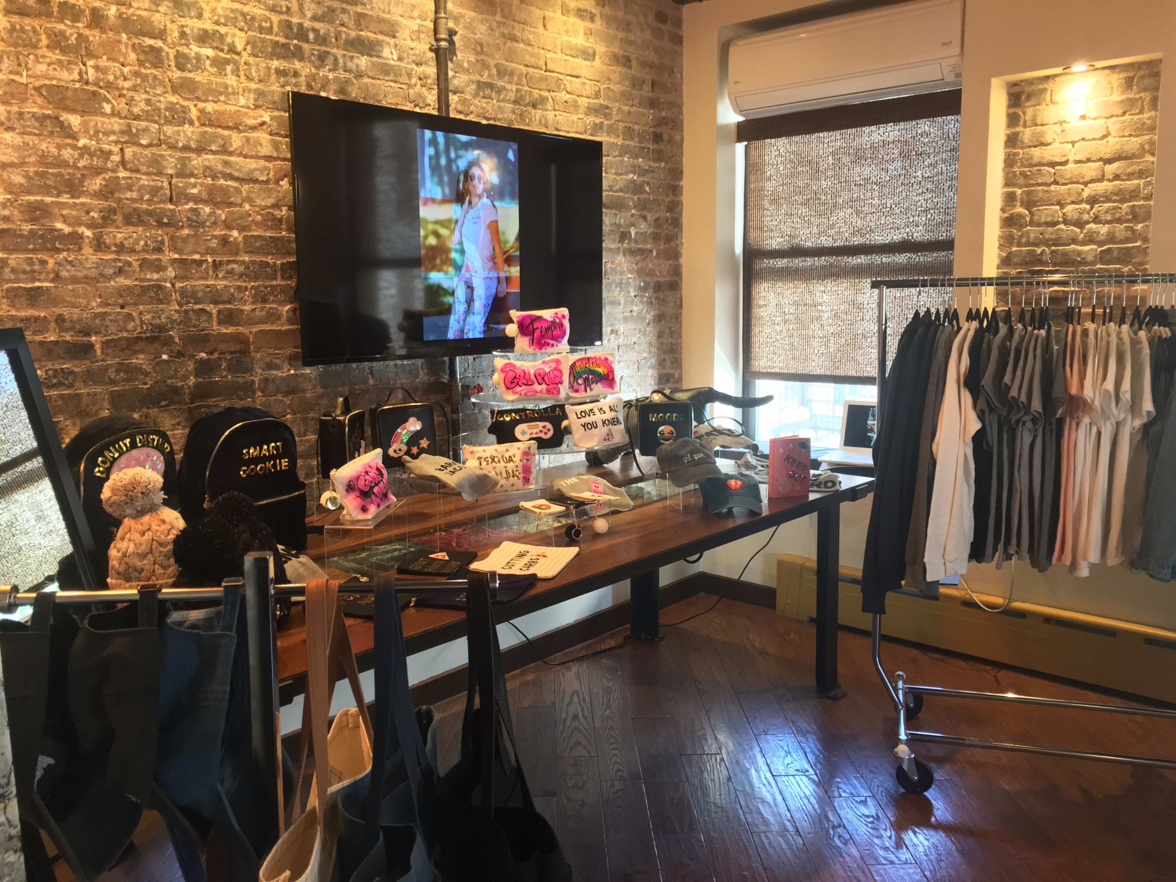 A display area features clothing and accessories on a wooden table and rack, with a large television showing a model wearing the apparel against a backdrop.
