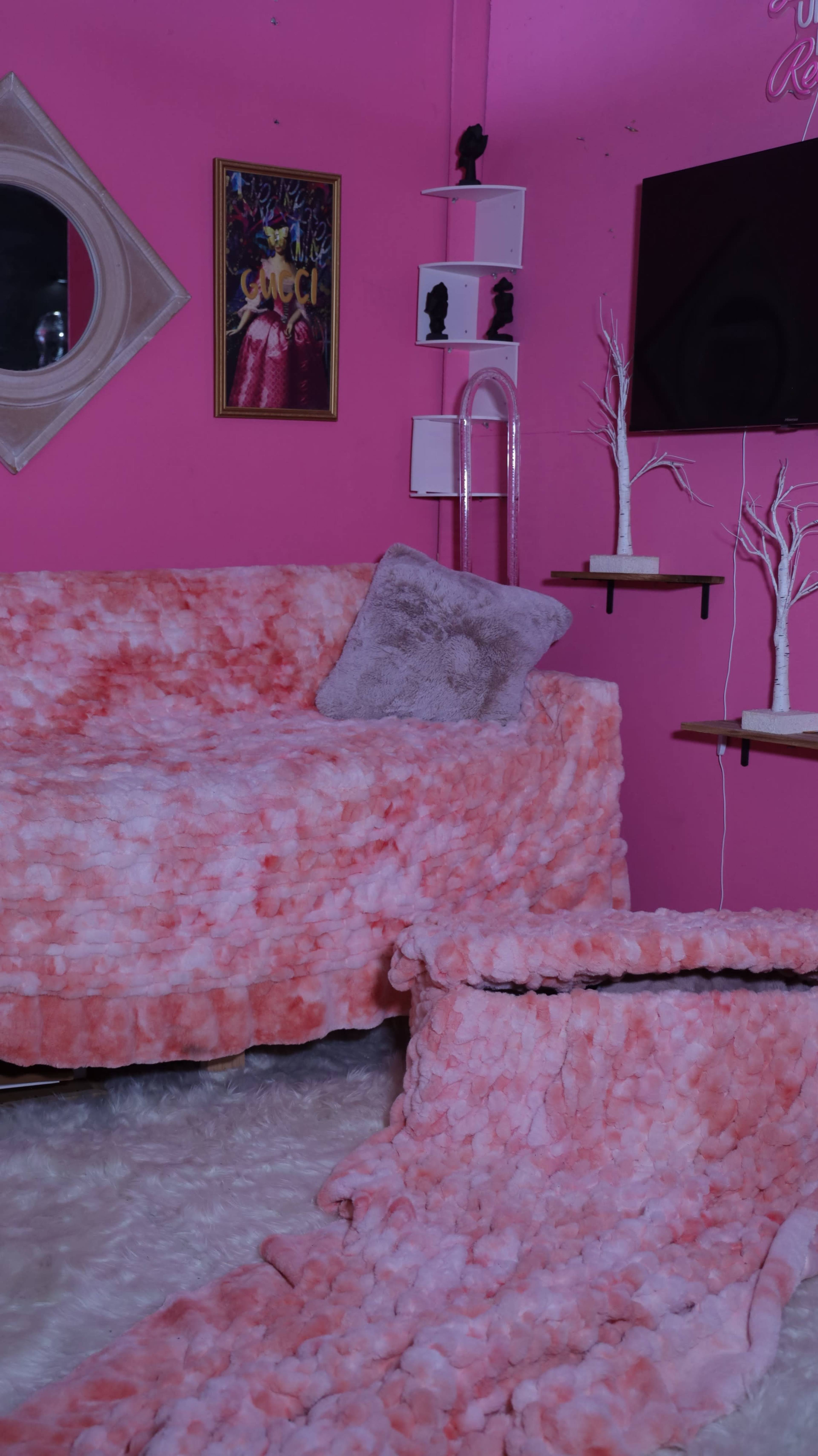 The image shows a pink-themed room featuring a couch and a coffee table covered in textured fabric, with white decorative trees and a mirror on the walls.