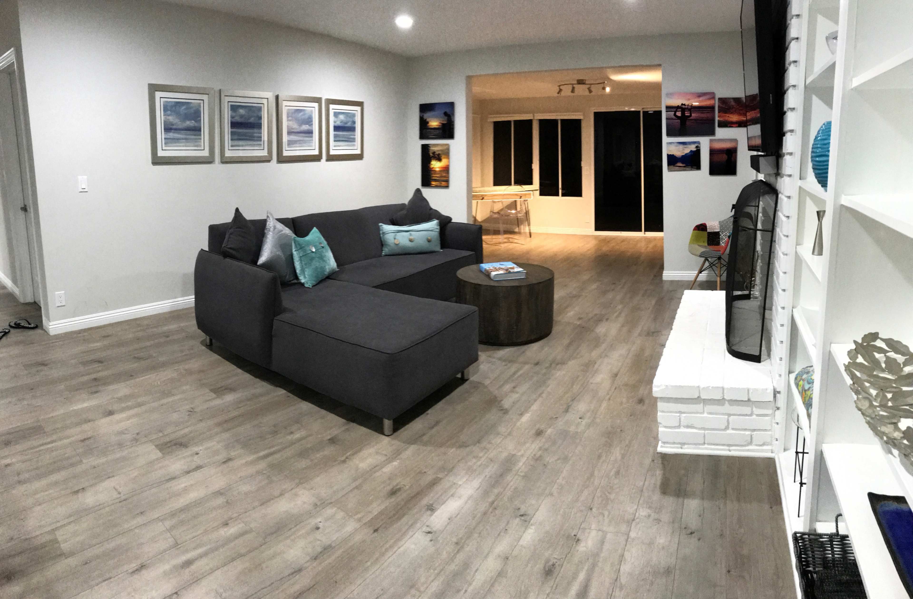 A modern living room featuring a gray sectional sofa, a circular coffee table, and artwork on the walls, with large windows leading to an outdoor area.