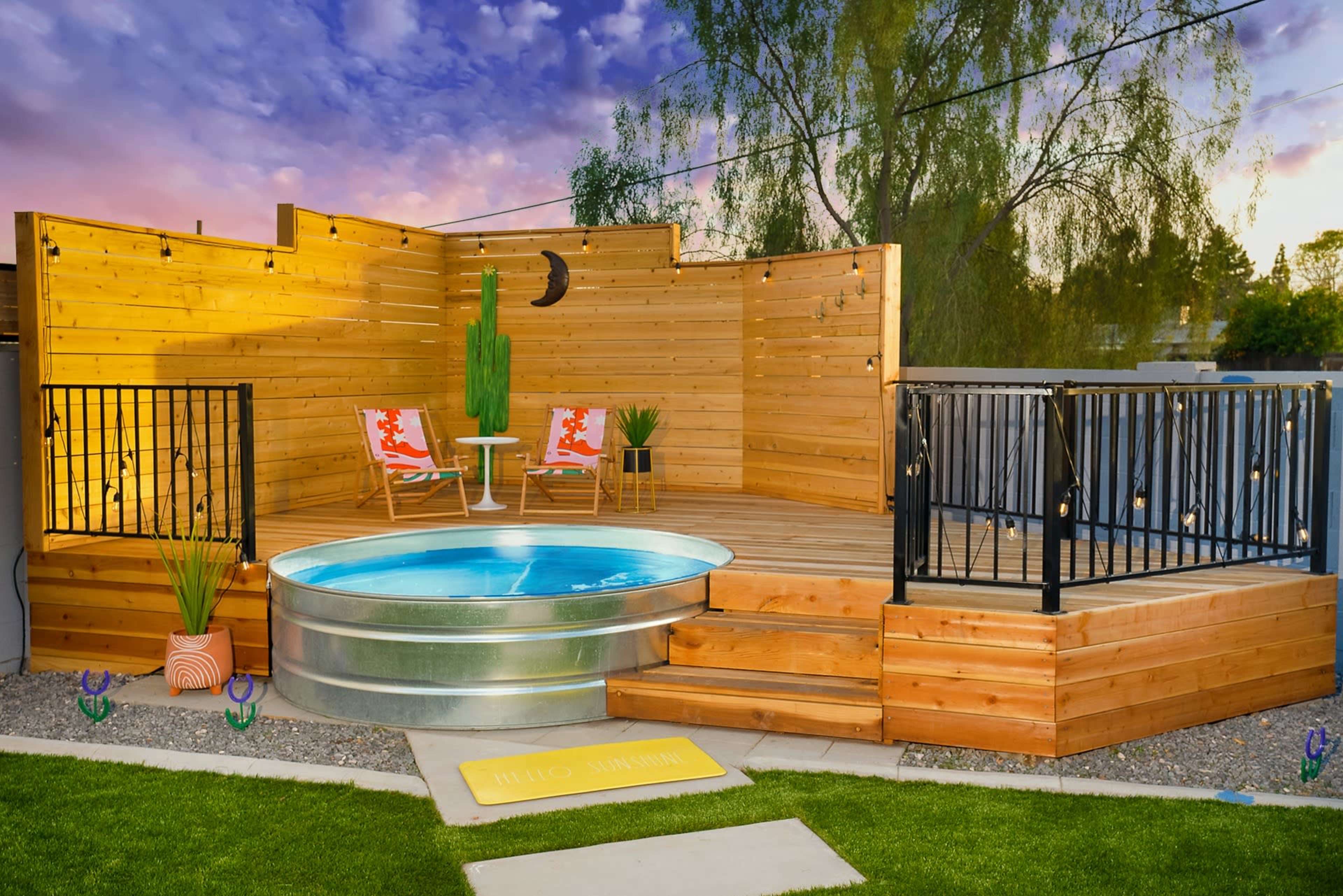 A wooden deck featuring a circular above-ground pool, surrounded by planters and chairs, with a sunset sky in the background.