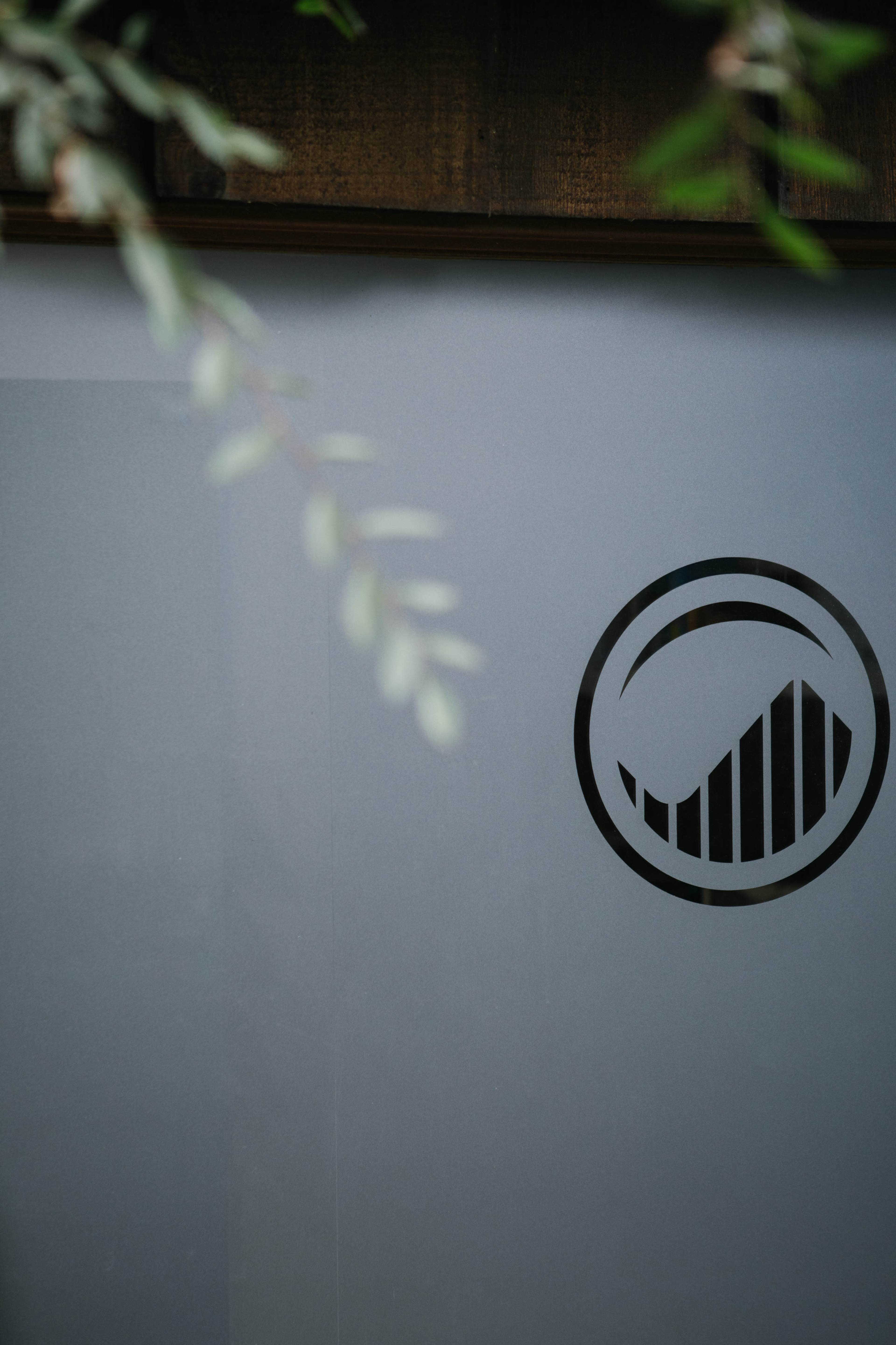 A partially obscured view of a glass surface featuring a circular logo with a stylized wave design.