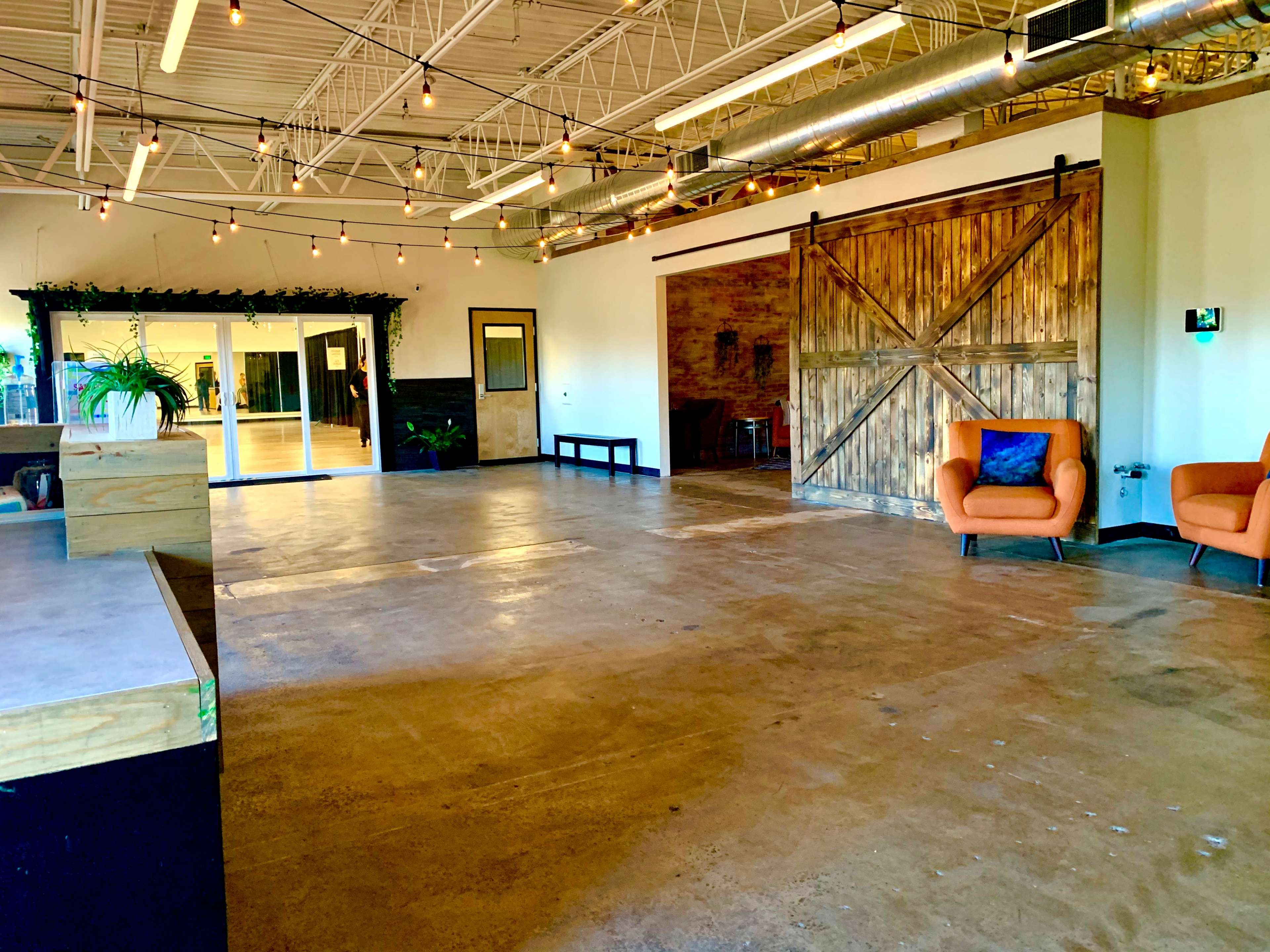 The image shows an empty indoor space featuring a polished concrete floor, a large sliding barn door, and a cozy orange armchair.