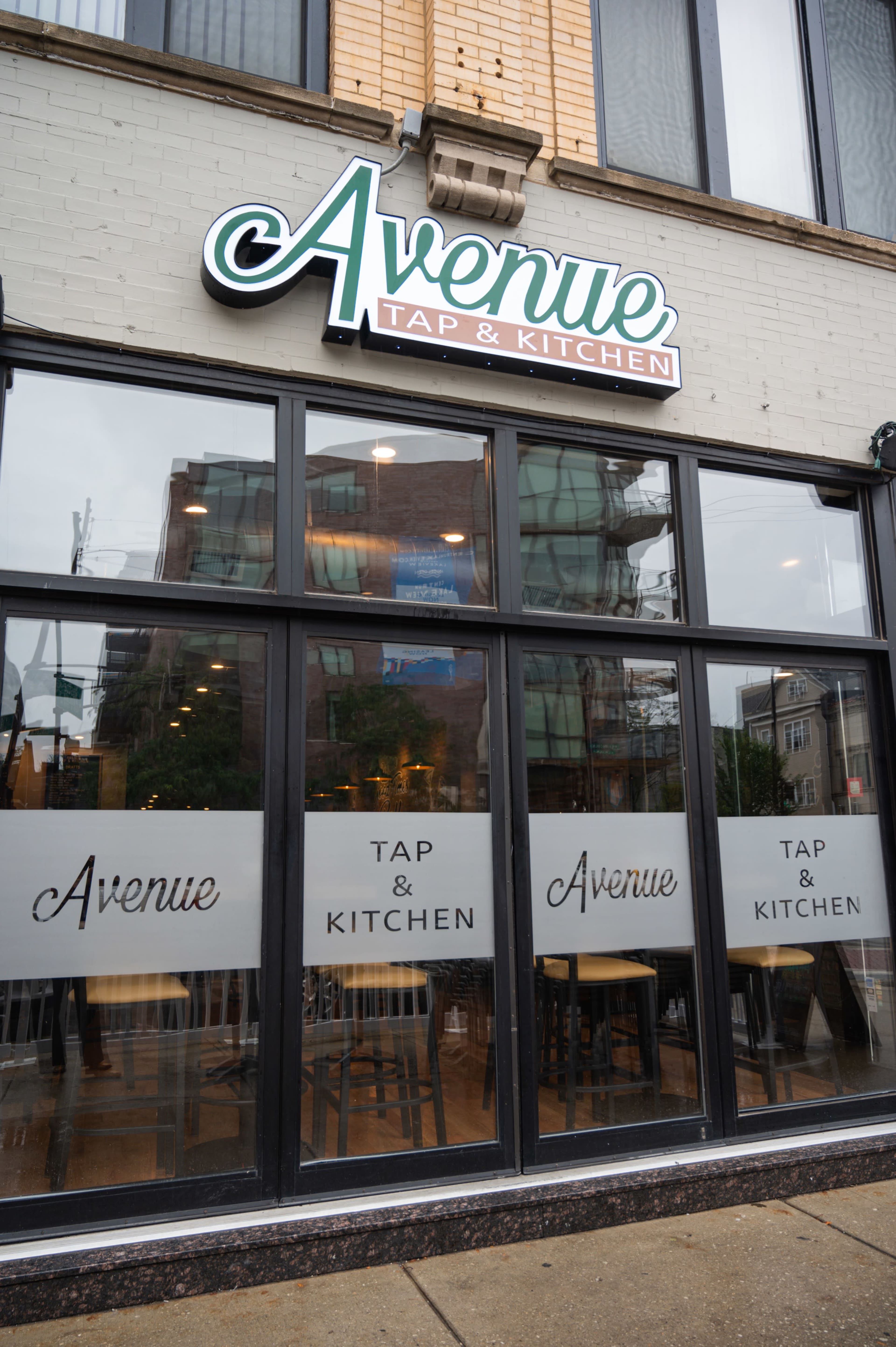 The image shows the exterior of a restaurant called "Avenue Tap & Kitchen," featuring large front windows with the restaurant's name and an inviting interior.