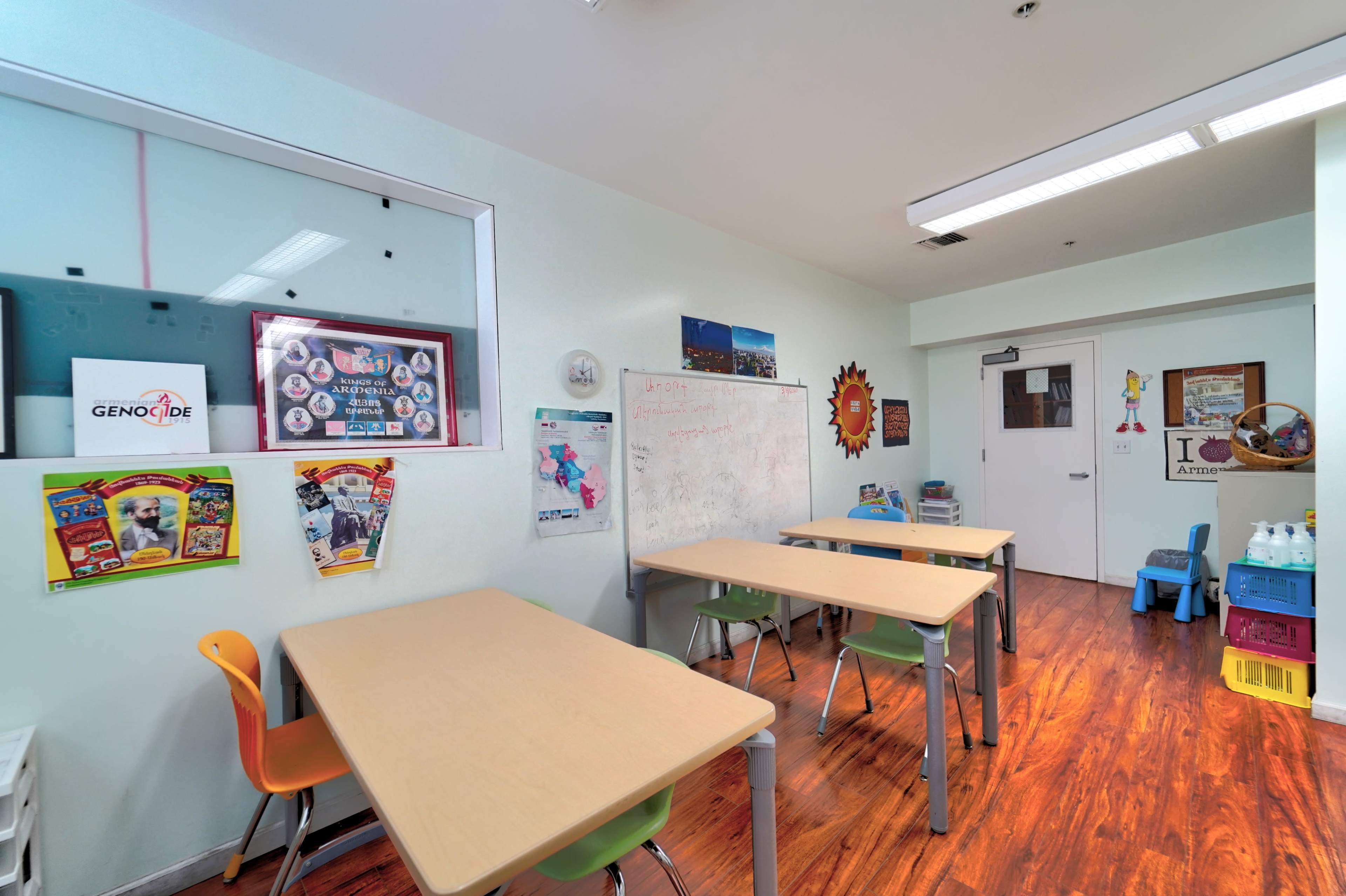 A classroom with four tables and chairs, whiteboards, and various educational posters on the walls.