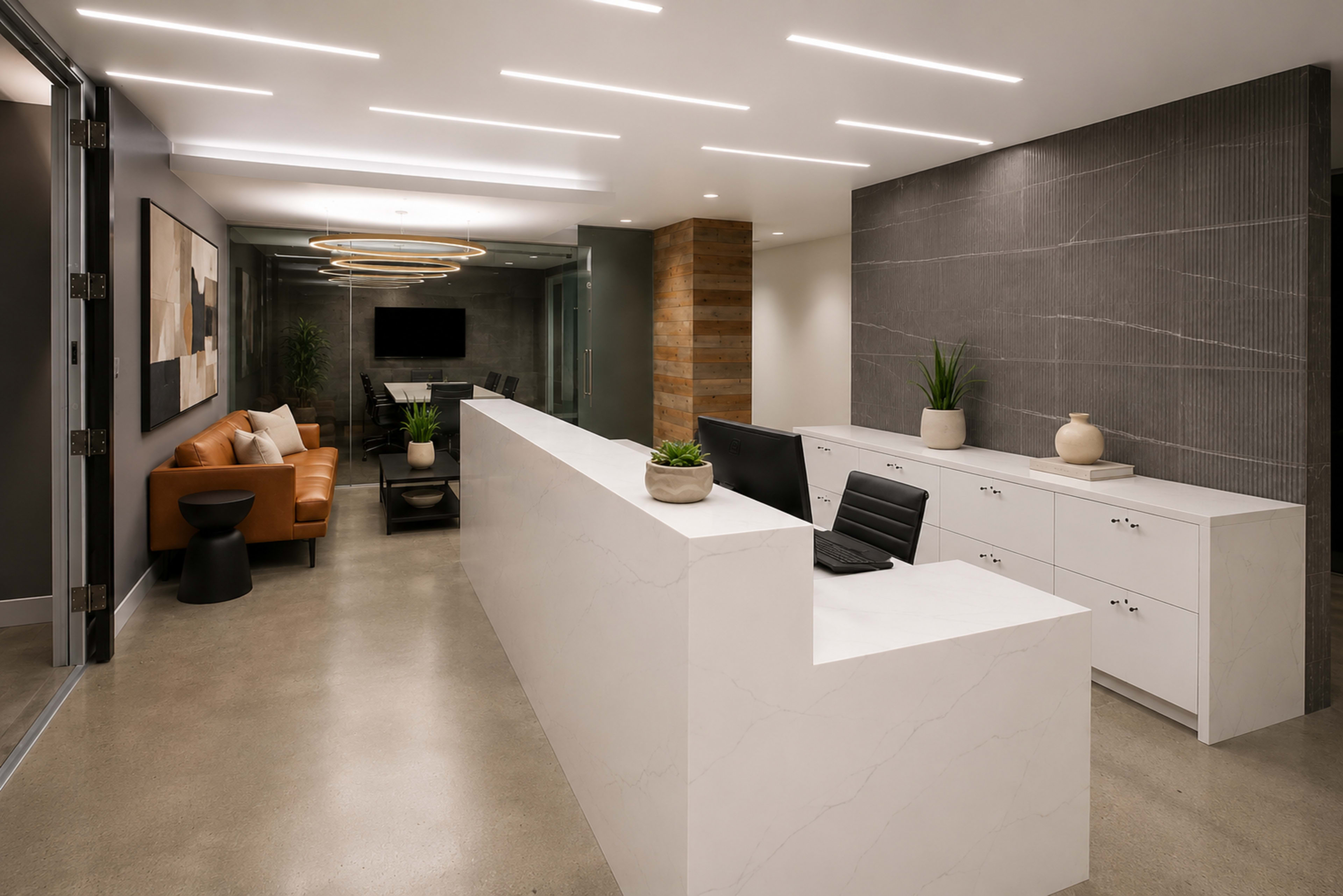The image shows a modern office reception area featuring a sleek white front desk, a brown leather sofa, and a conference room visible in the background.