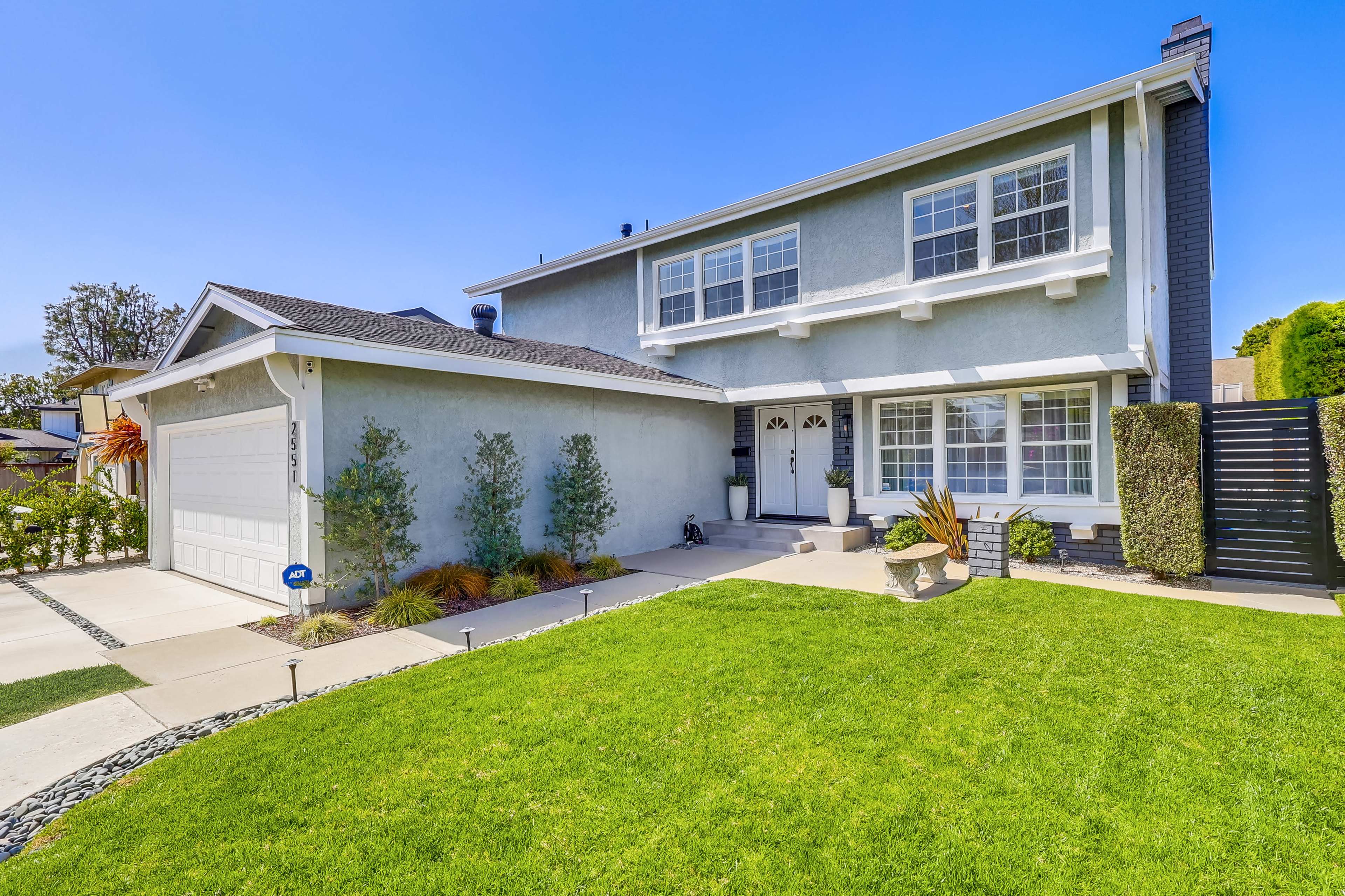 The image shows a two-story house with a light blue exterior, a neatly maintained front yard, and a concrete driveway.