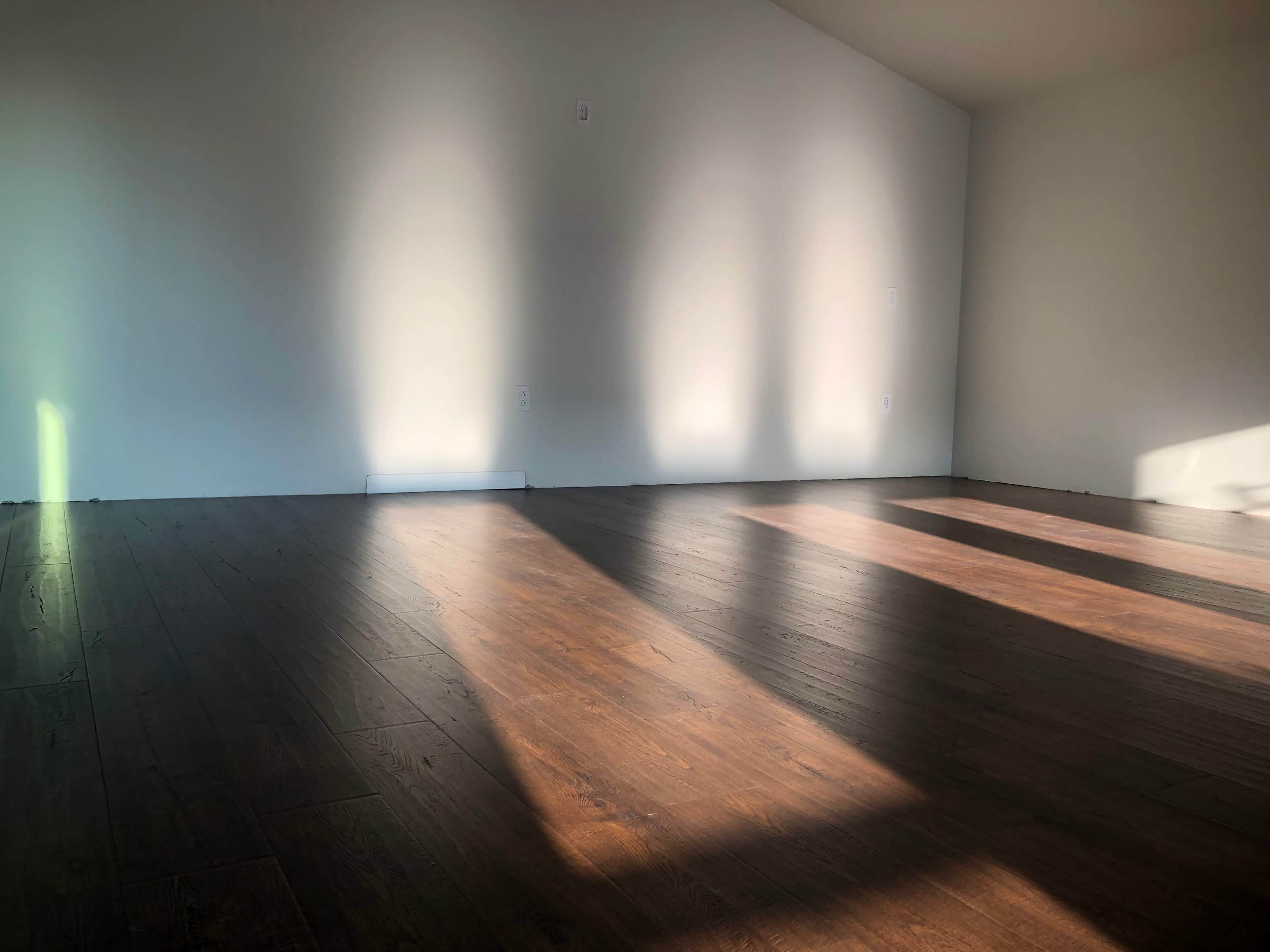 A sparsely furnished room with wooden flooring and sunlight casting shadows on the walls.