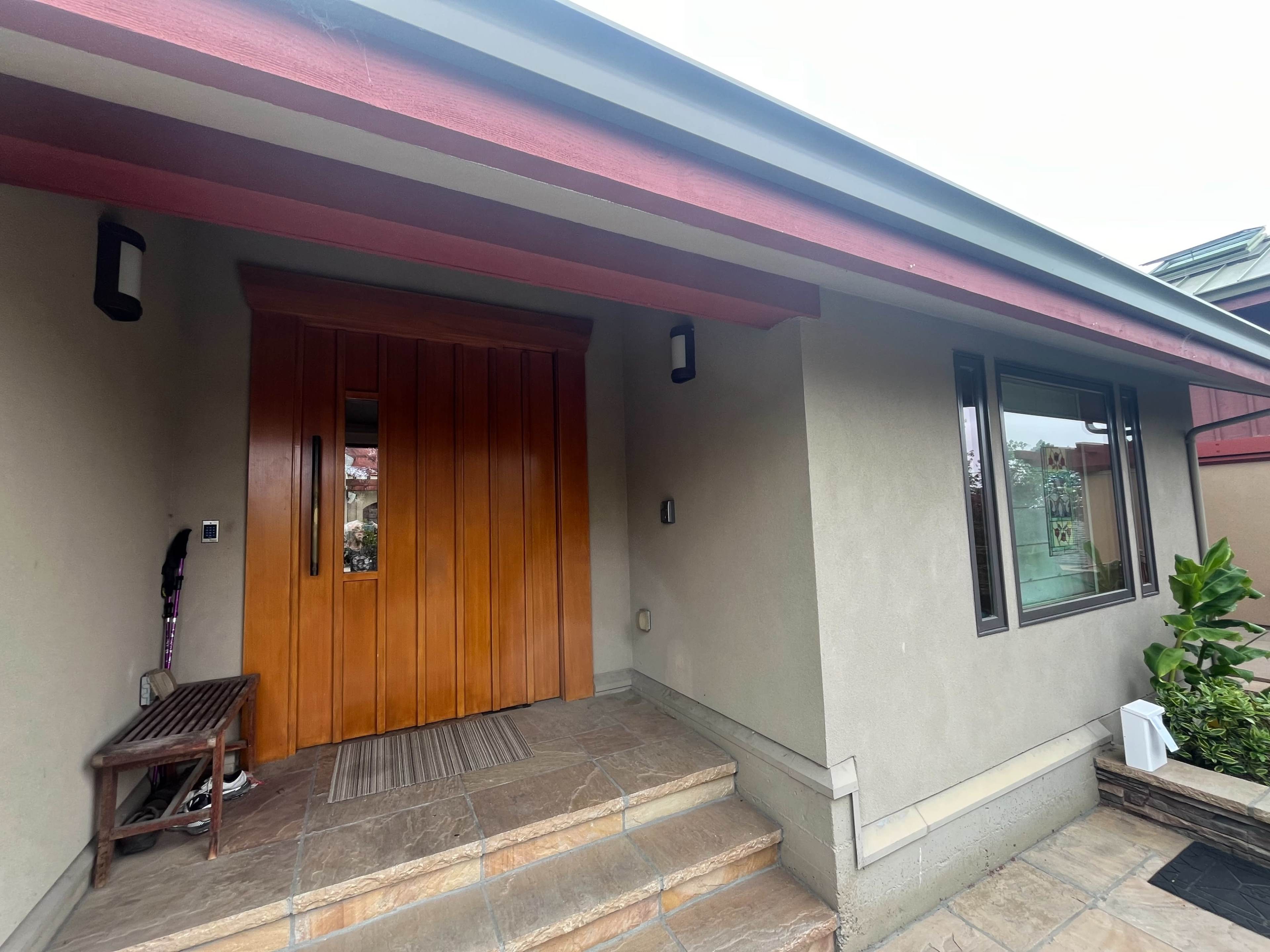 A house entrance with wooden double doors, a stone pathway, and a bench beside the door.