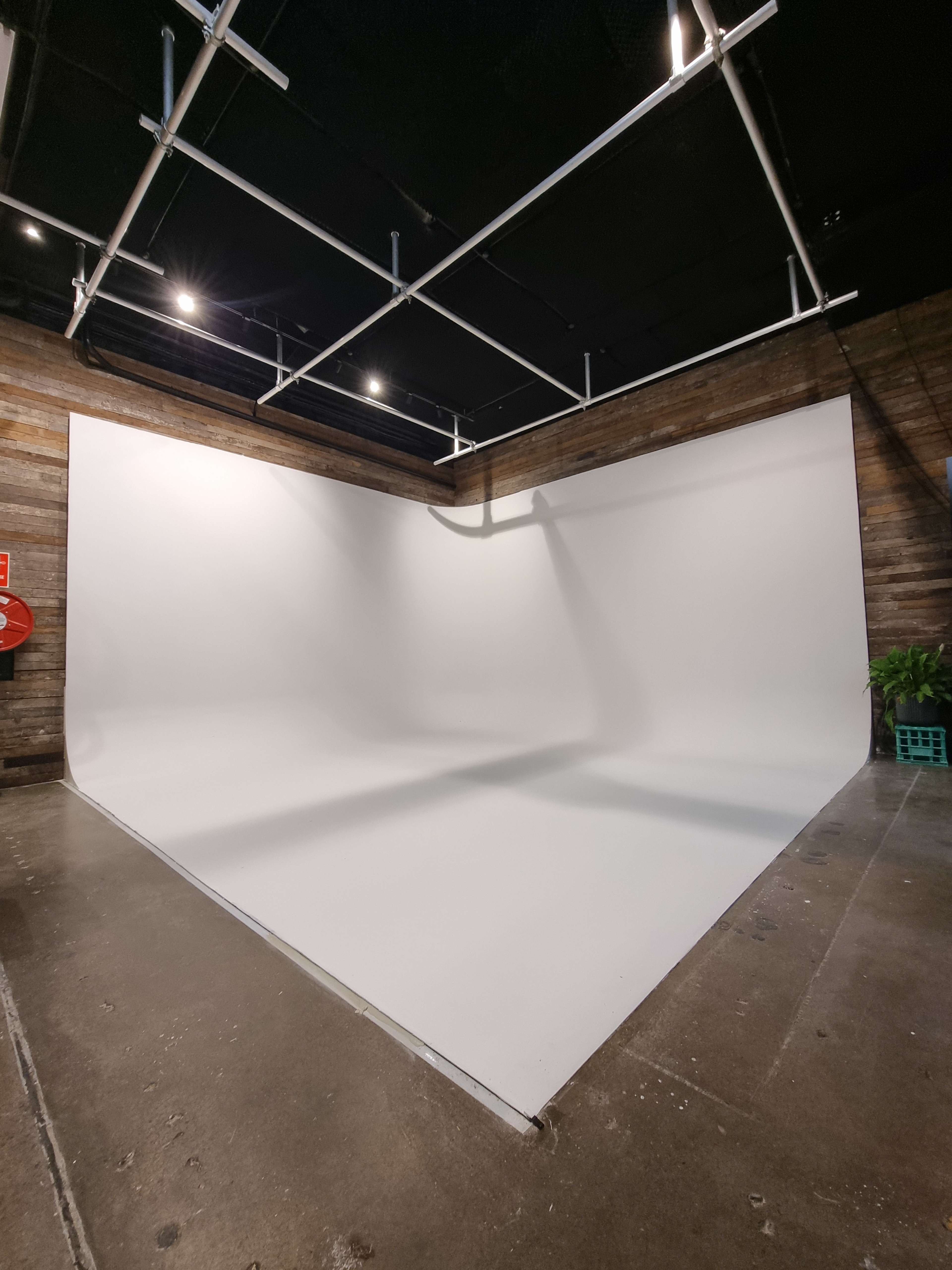 The image shows a spacious photography studio with a large white backdrop and wooden walls.