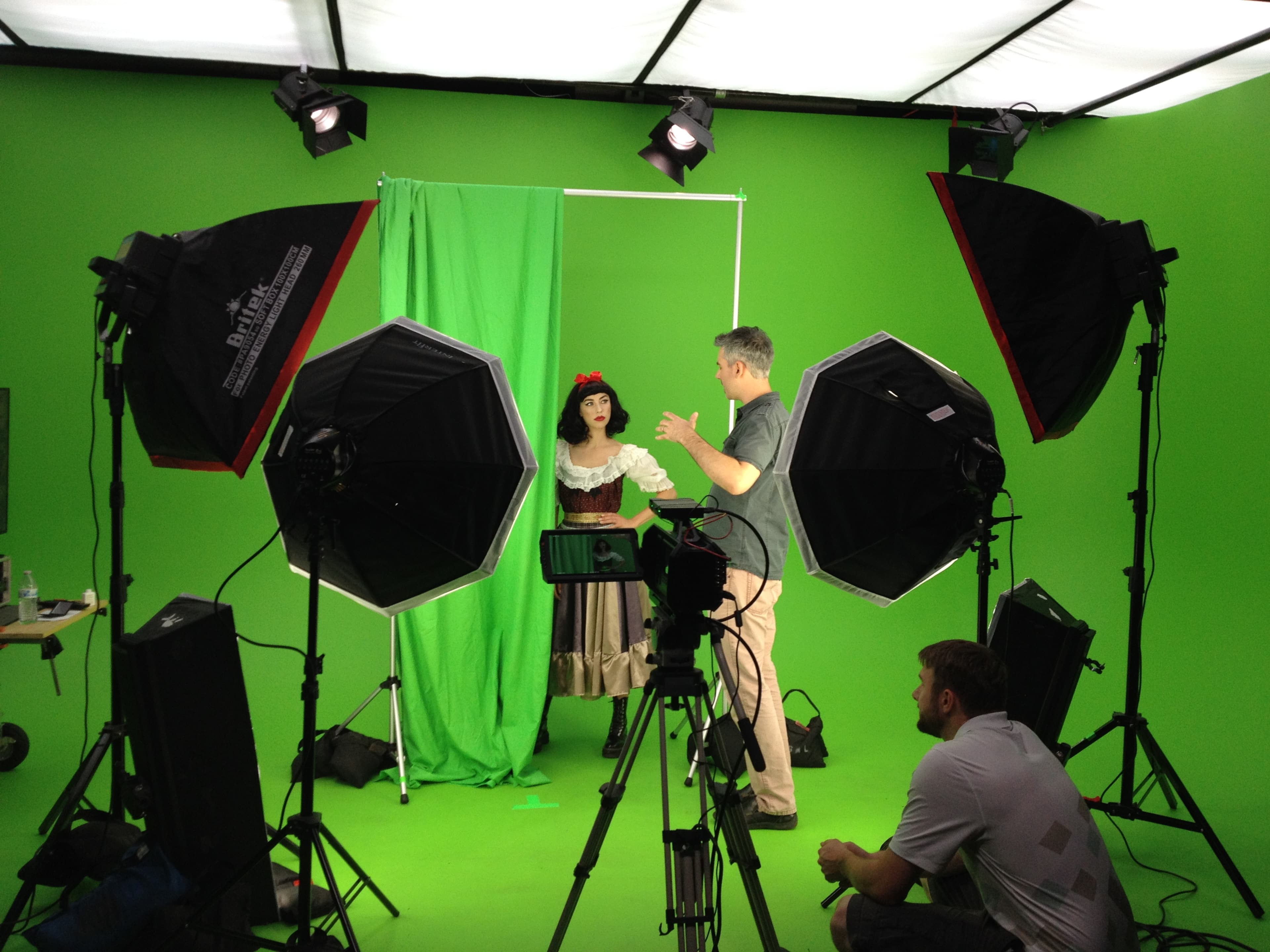 A person gestures towards a mannequin dressed in costume on a set with green screens and multiple lighting setups.