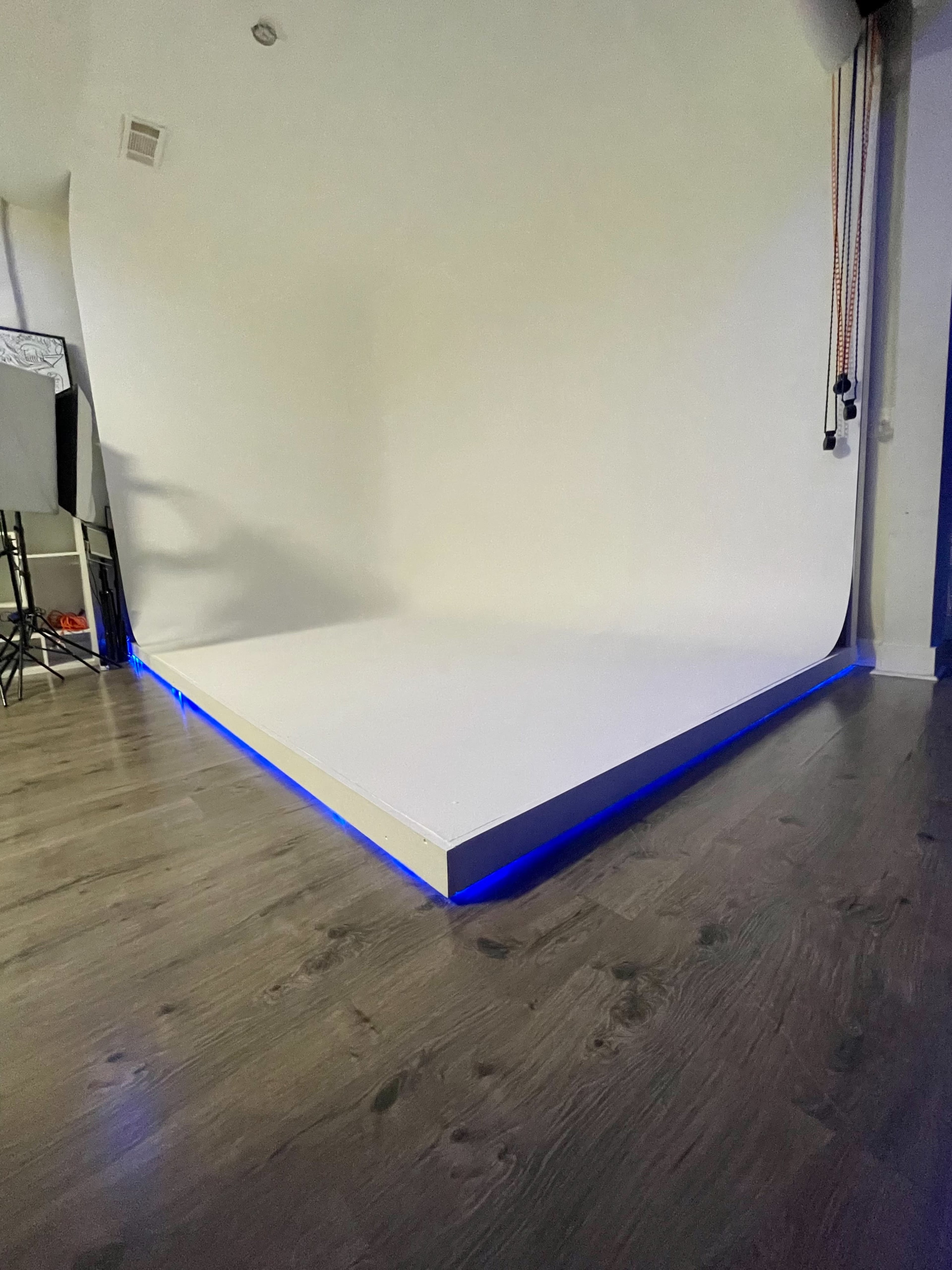 A photography studio featuring a white backdrop on a raised platform with blue LED lighting along the edges.