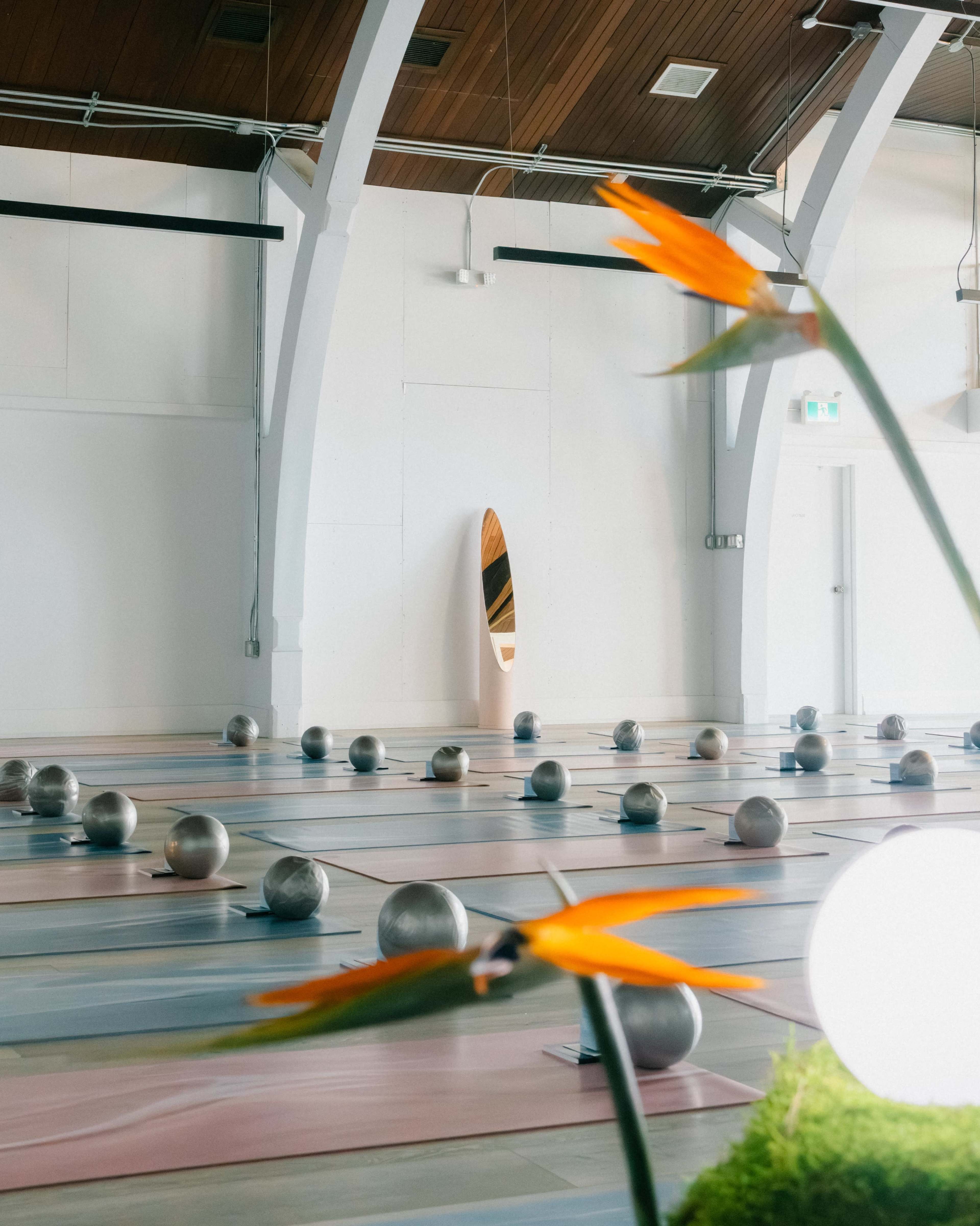 The image shows an empty yoga studio with exercise mats arranged in rows and a surfboard leaning against the wall.