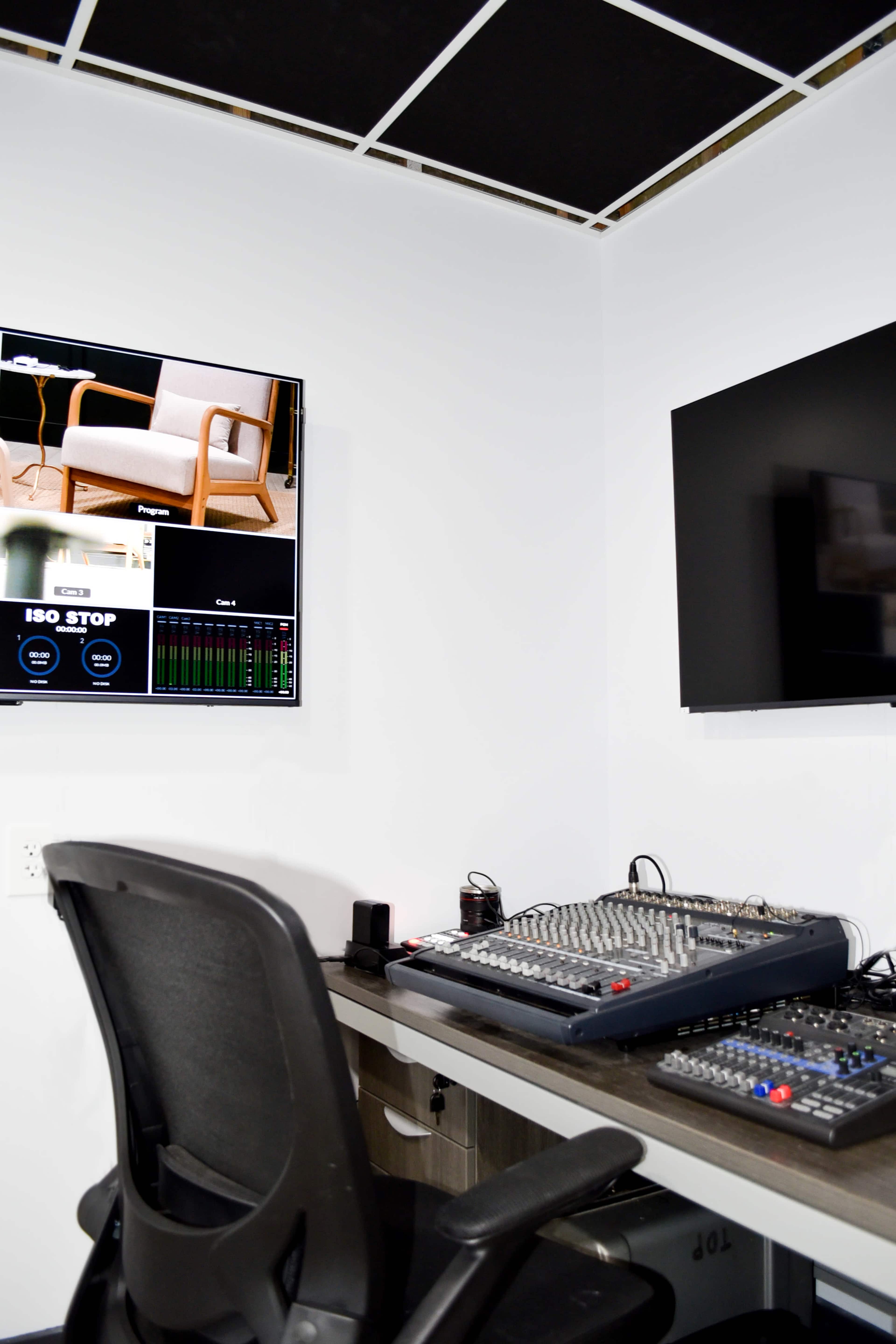 The image shows a sound mixing desk and two monitors mounted on the wall in a recording studio or control room.