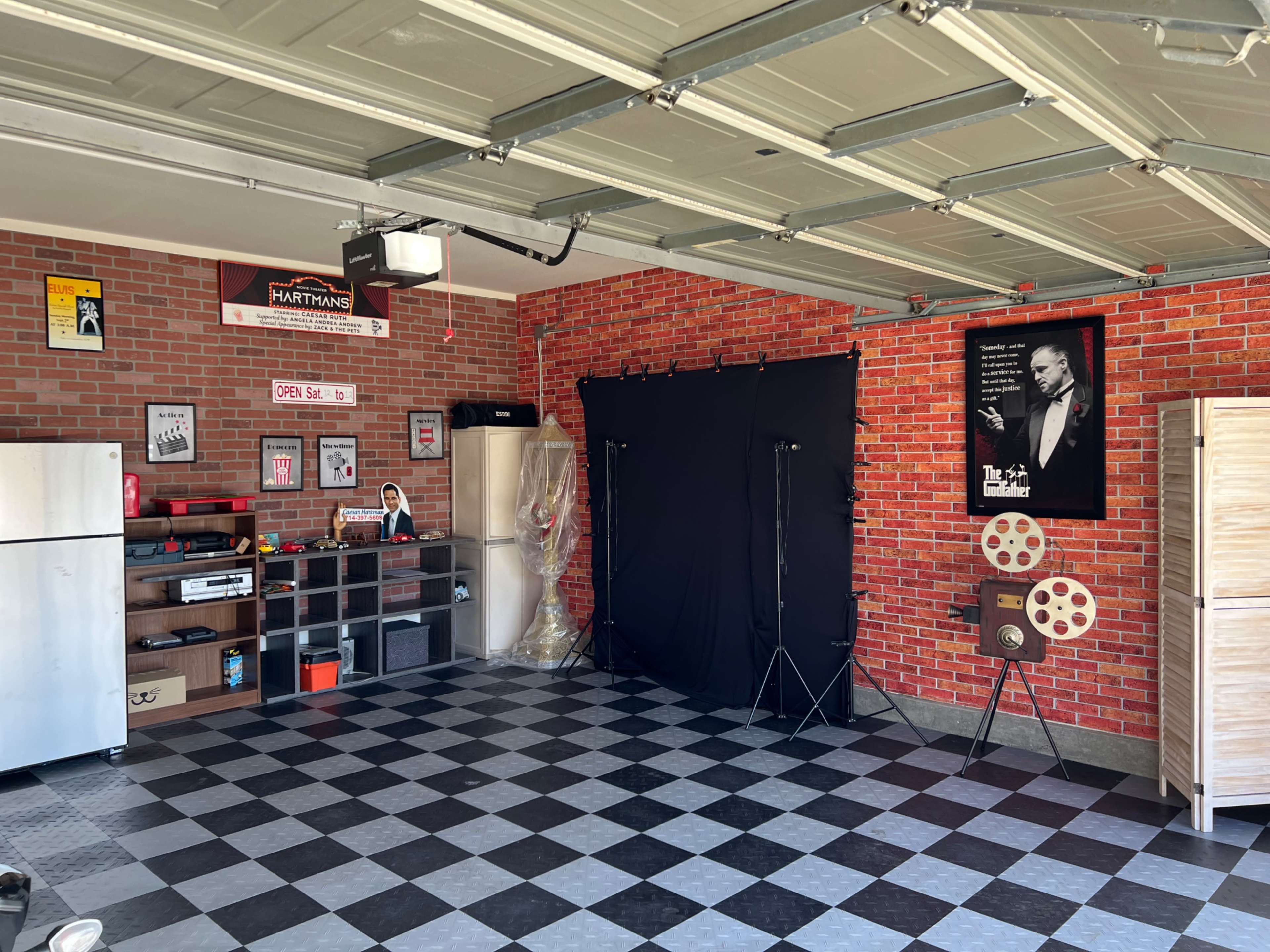 A garage with a brick-patterned wall, a checkered floor, and various decorations, including a movie-themed poster and a display of film reels.