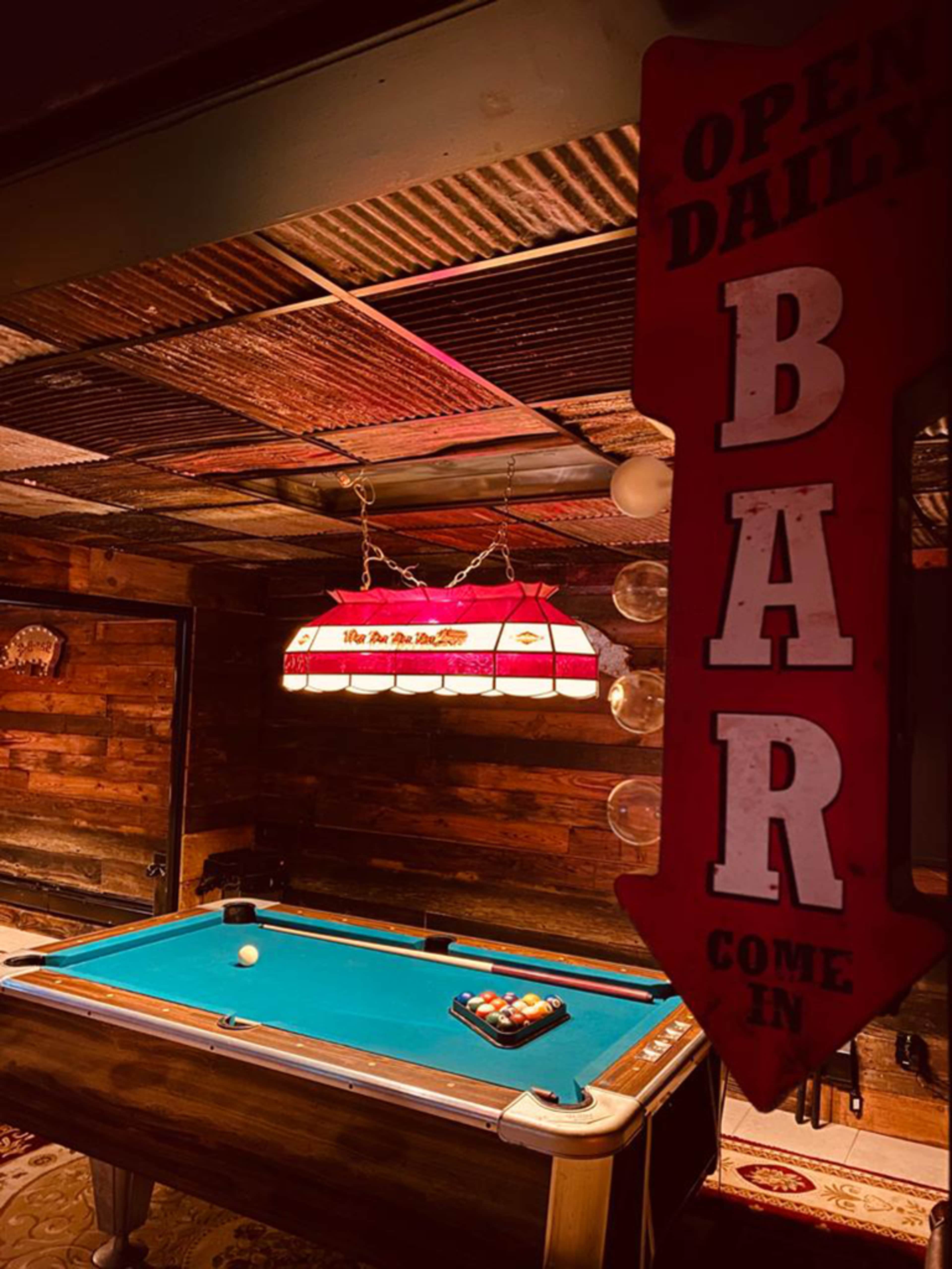 A dimly lit room with a pool table and a prominent sign indicating that the bar is open daily.