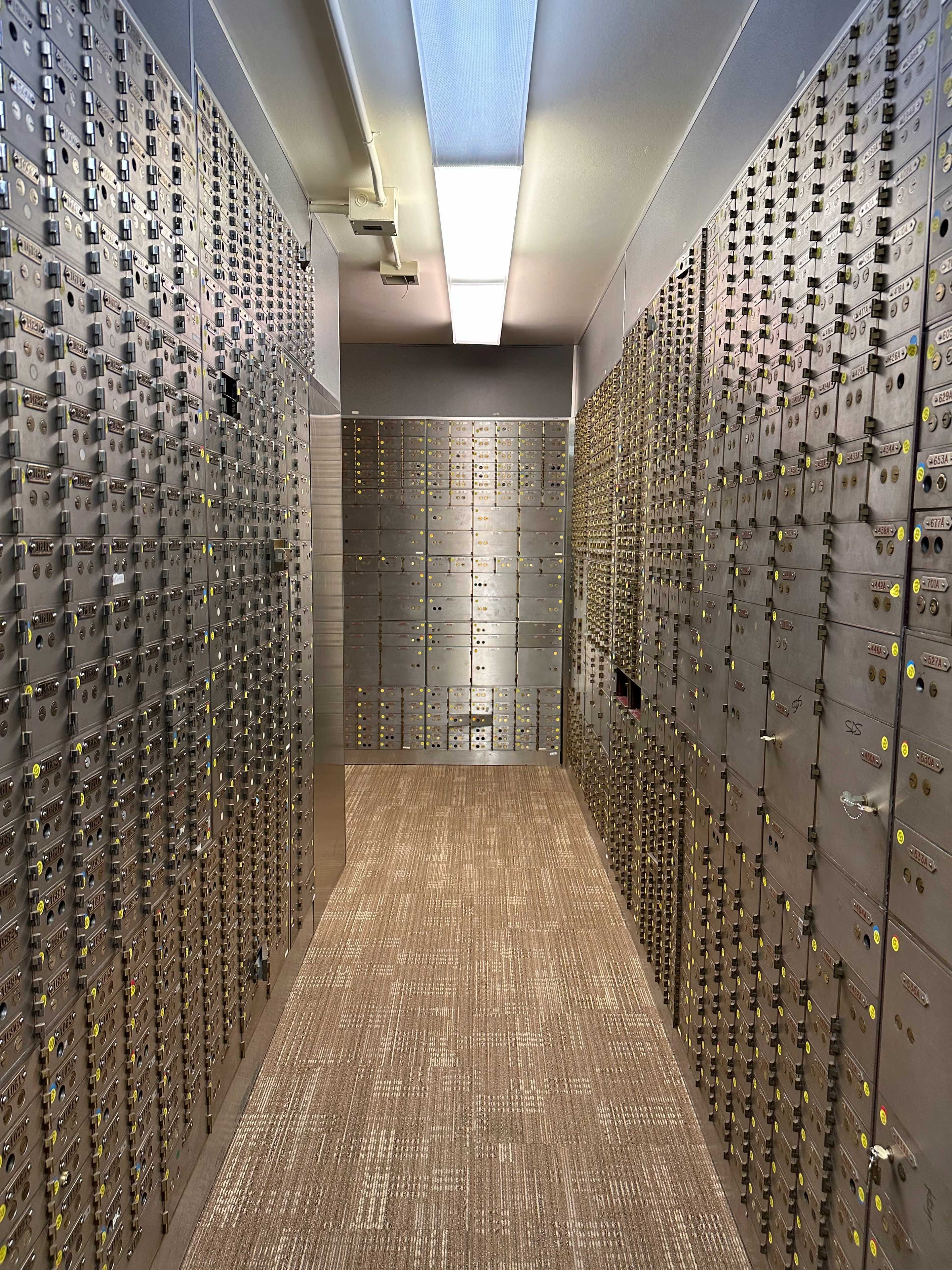 A vault room filled with numerous metallic safety deposit boxes arranged in rows on the walls.