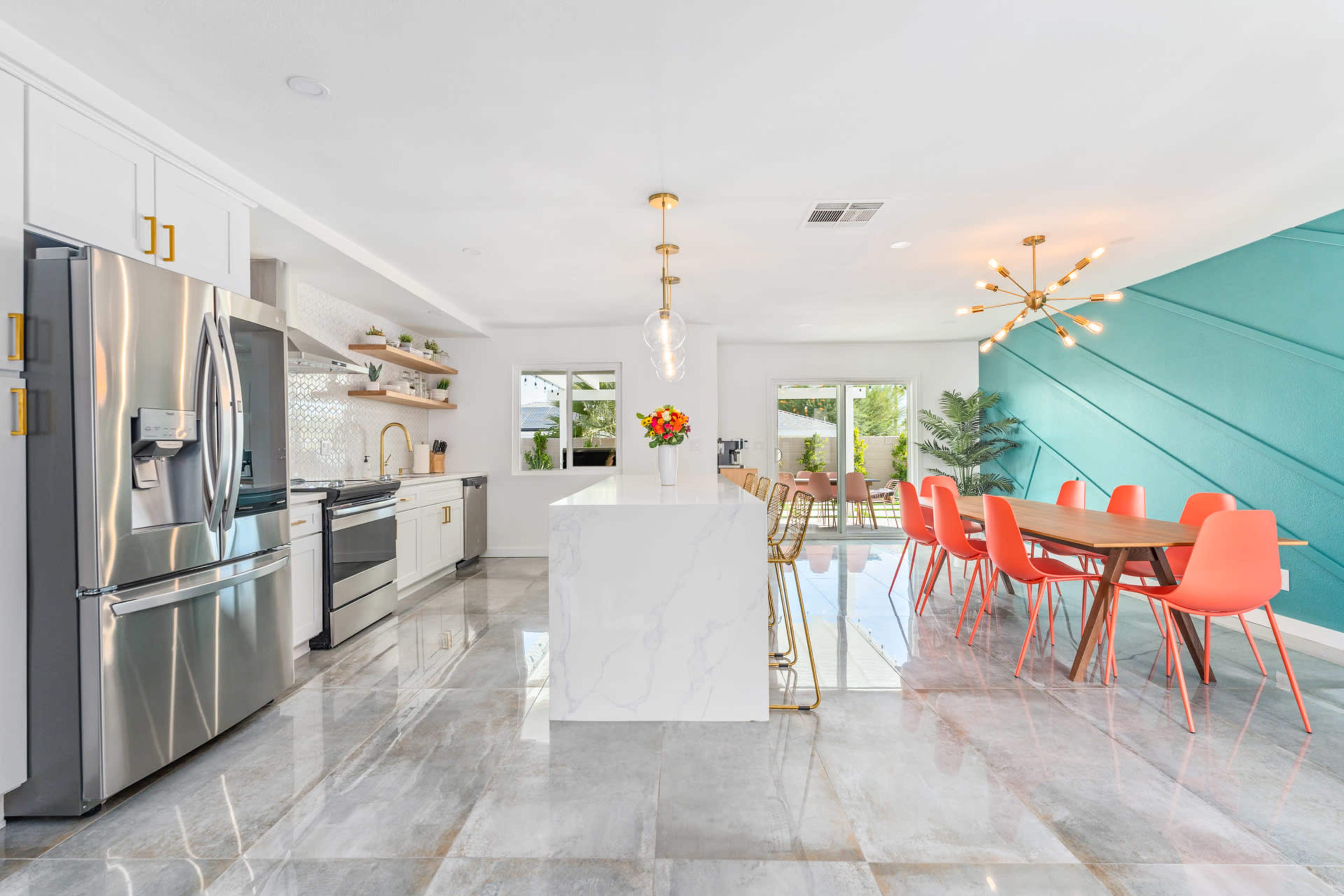 A modern kitchen and dining area featuring stainless steel appliances, marble countertops, and a dining table with colorful chairs.