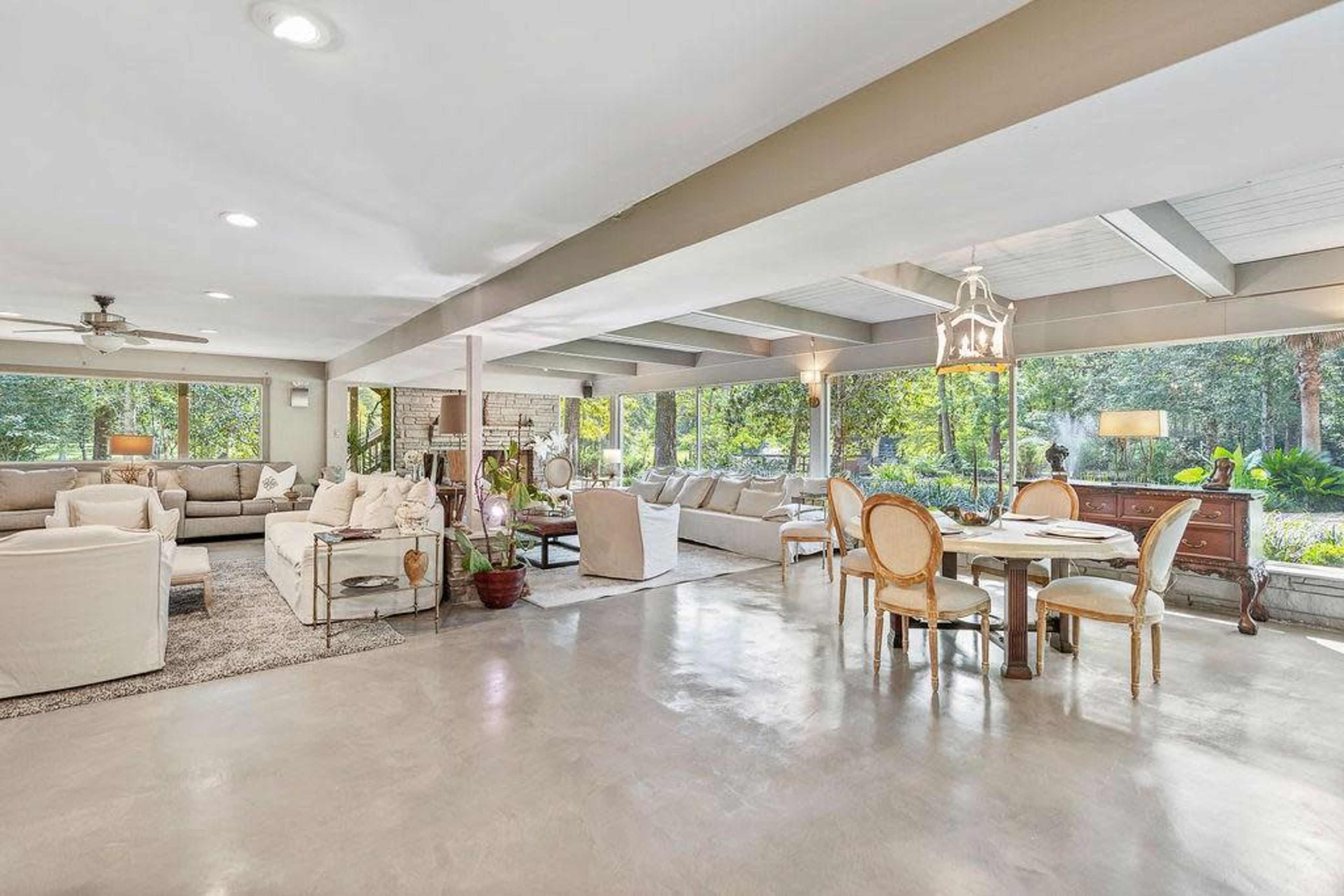 A spacious living area featuring a mix of seating arrangements, a dining table, and large windows overlooking a green landscape.